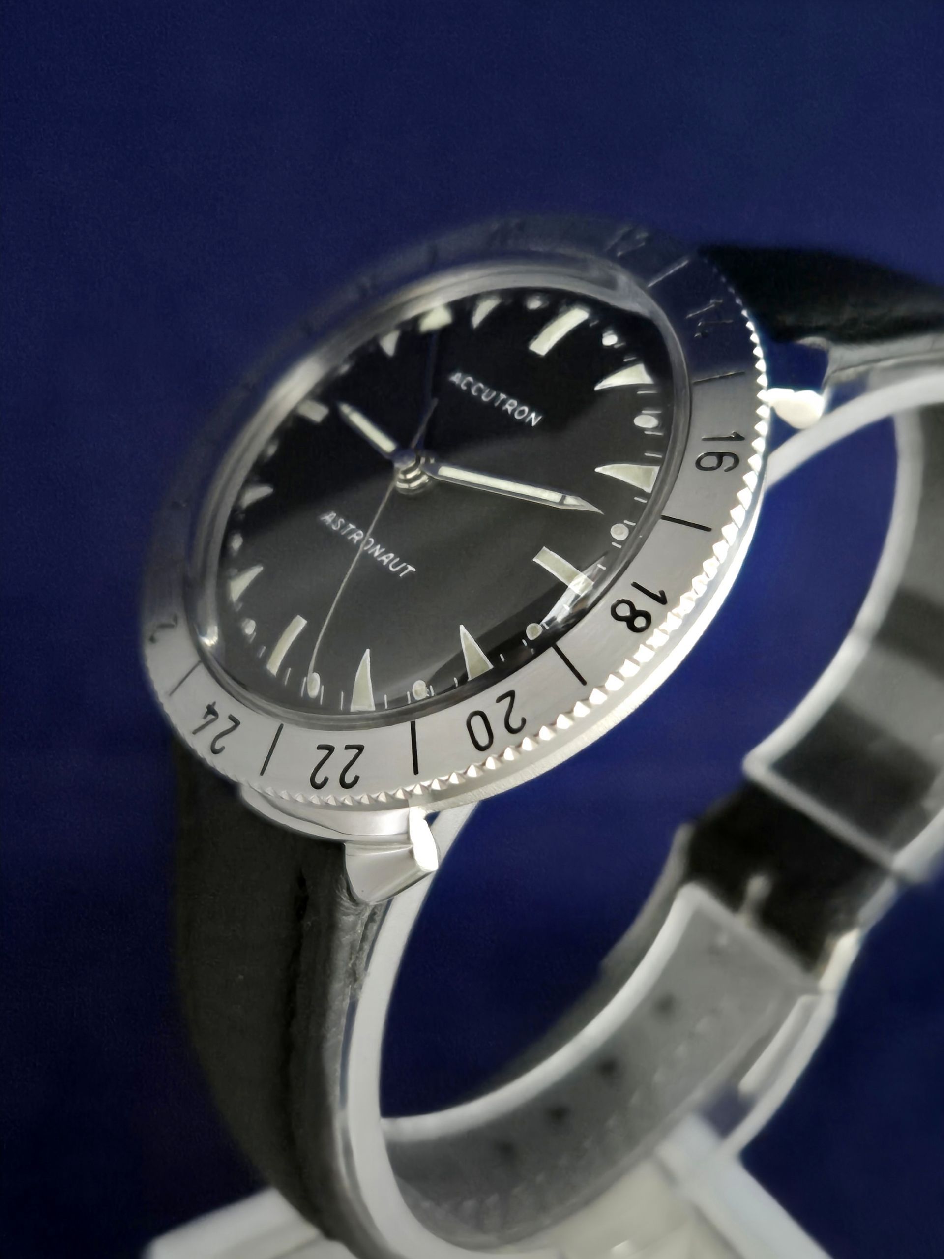 Silver wristwatch with black dial and black strap on a blue background
