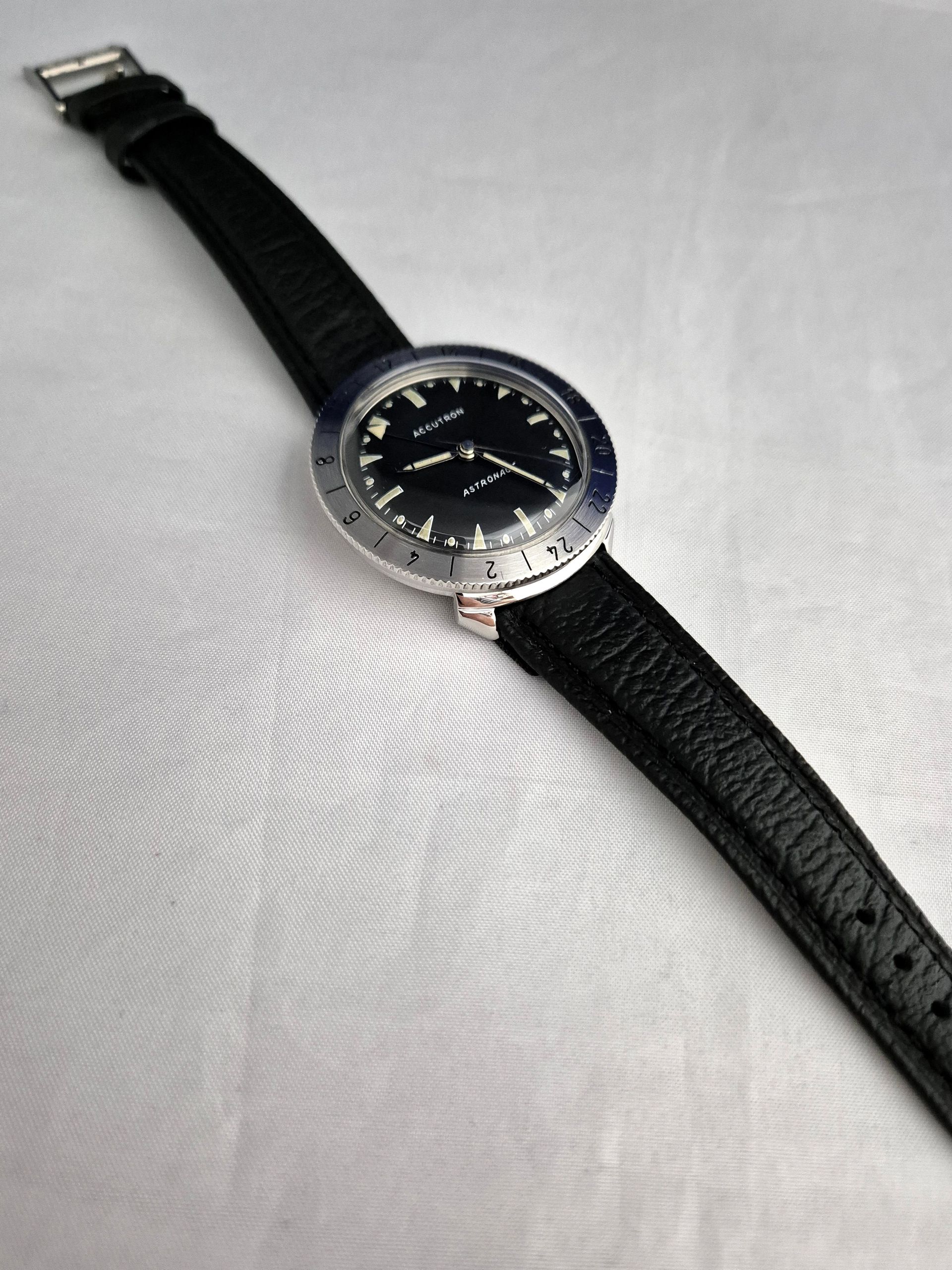 Black wristwatch with a silver bezel and black leather strap on a white surface