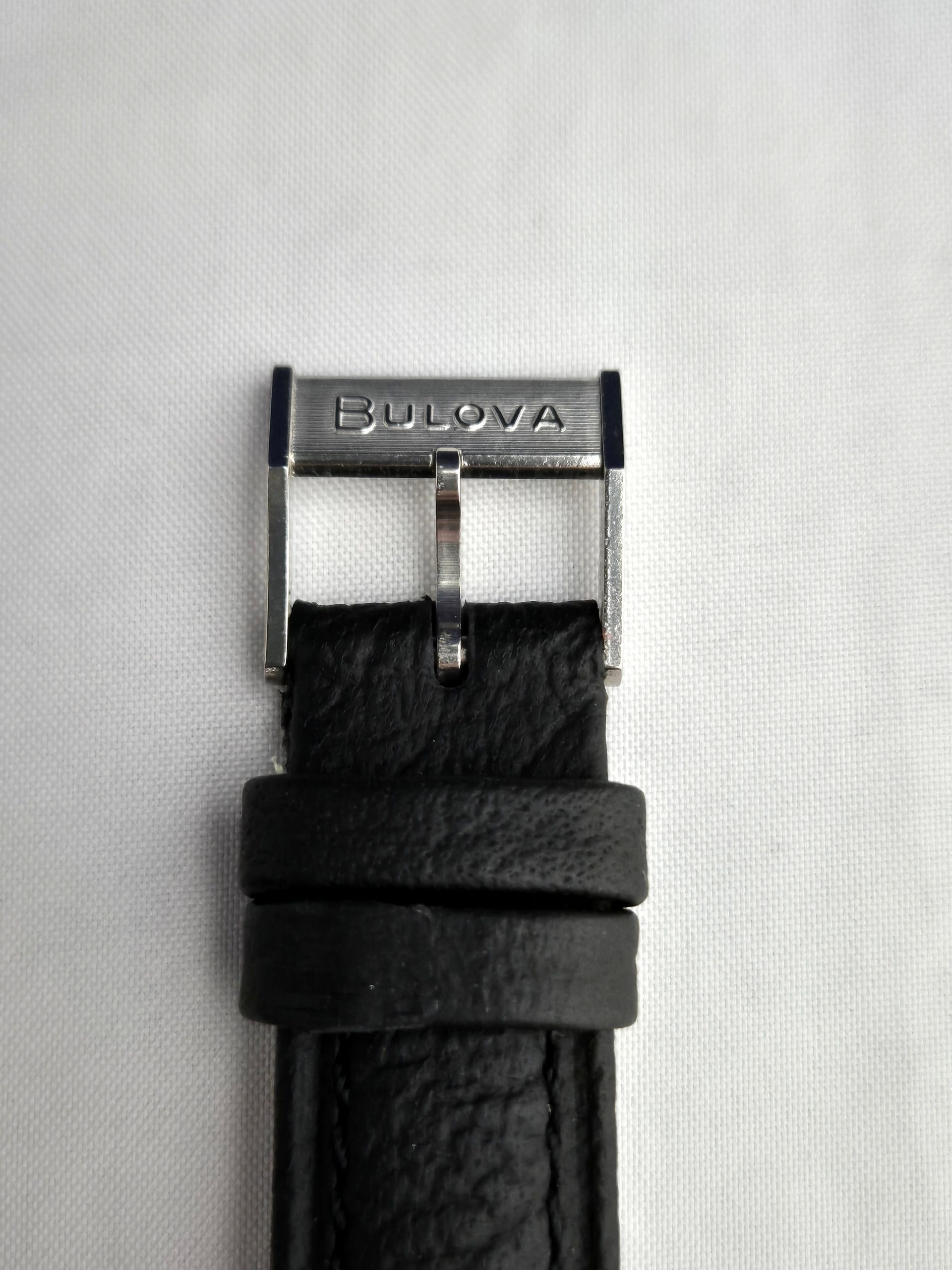 Black leather Bulova watch strap with silver buckle on a light background
