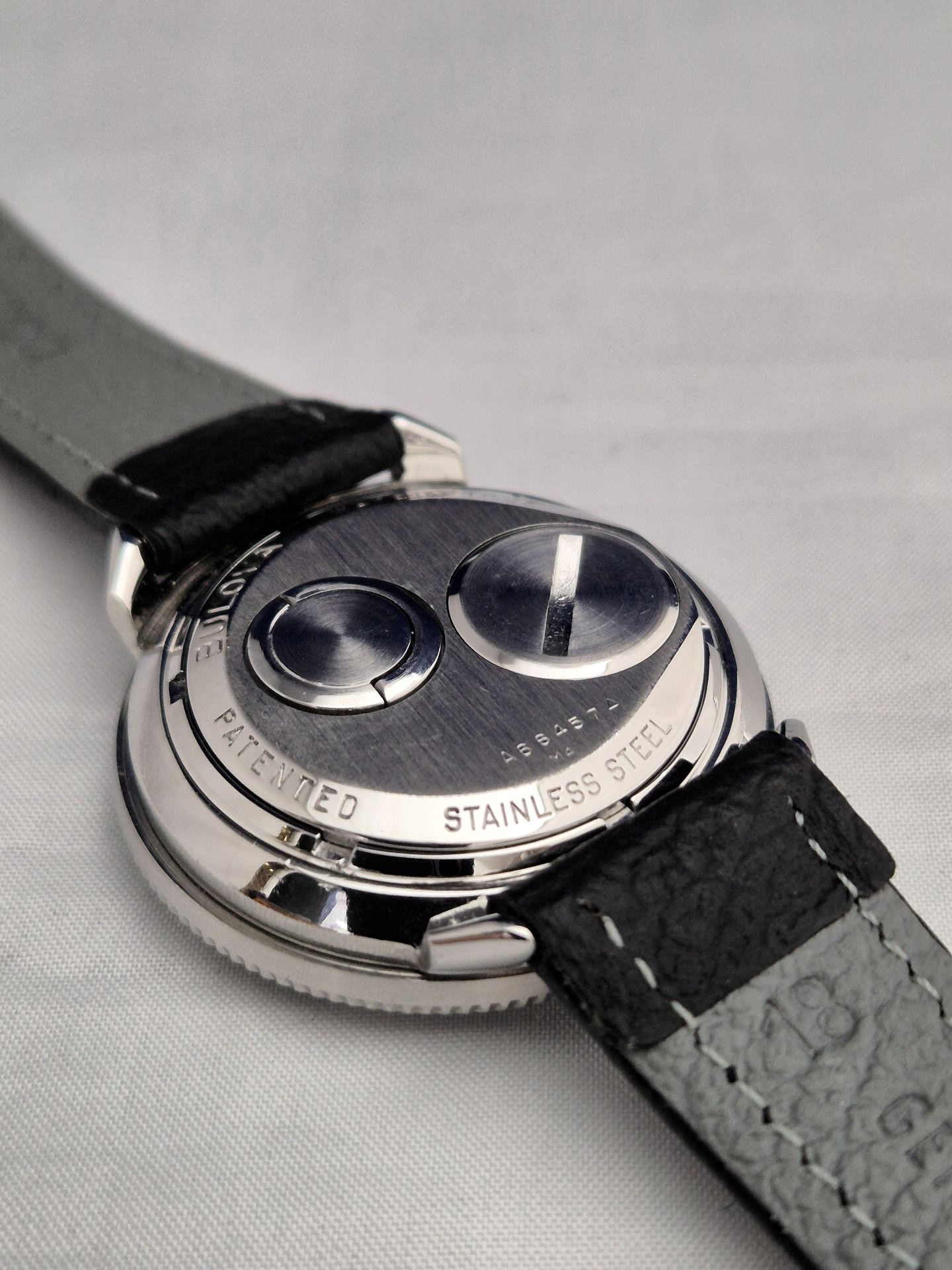 Close-up of a silver wristwatch with a black leather strap on a gray surface