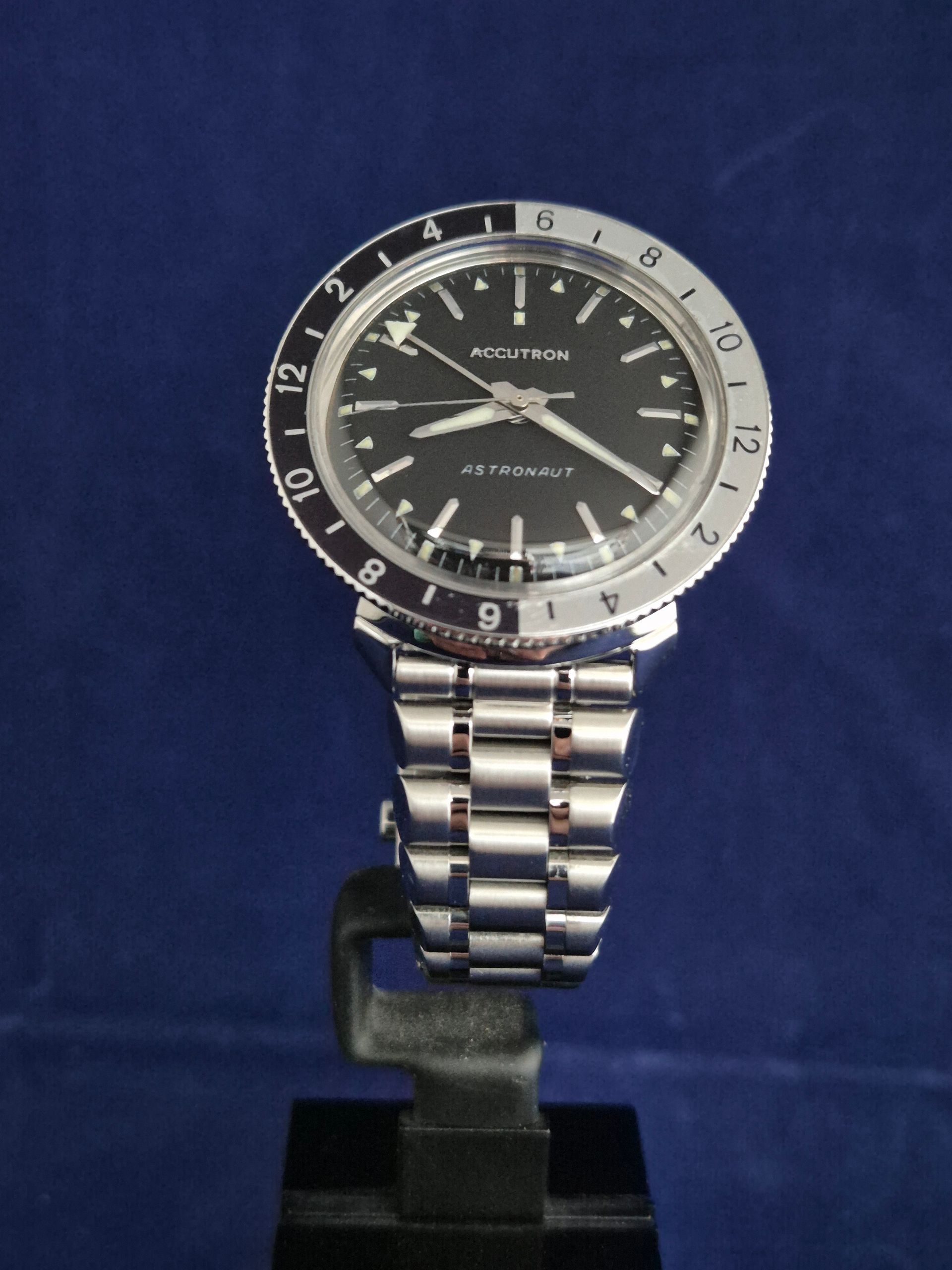 Silver wristwatch with black face on a stand against a dark blue background