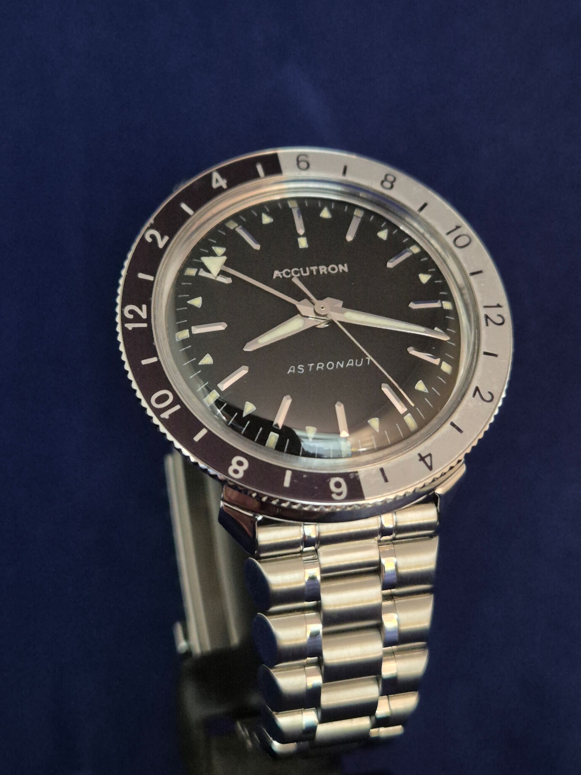 A silver wristwatch with a black face and metal band on a dark blue background