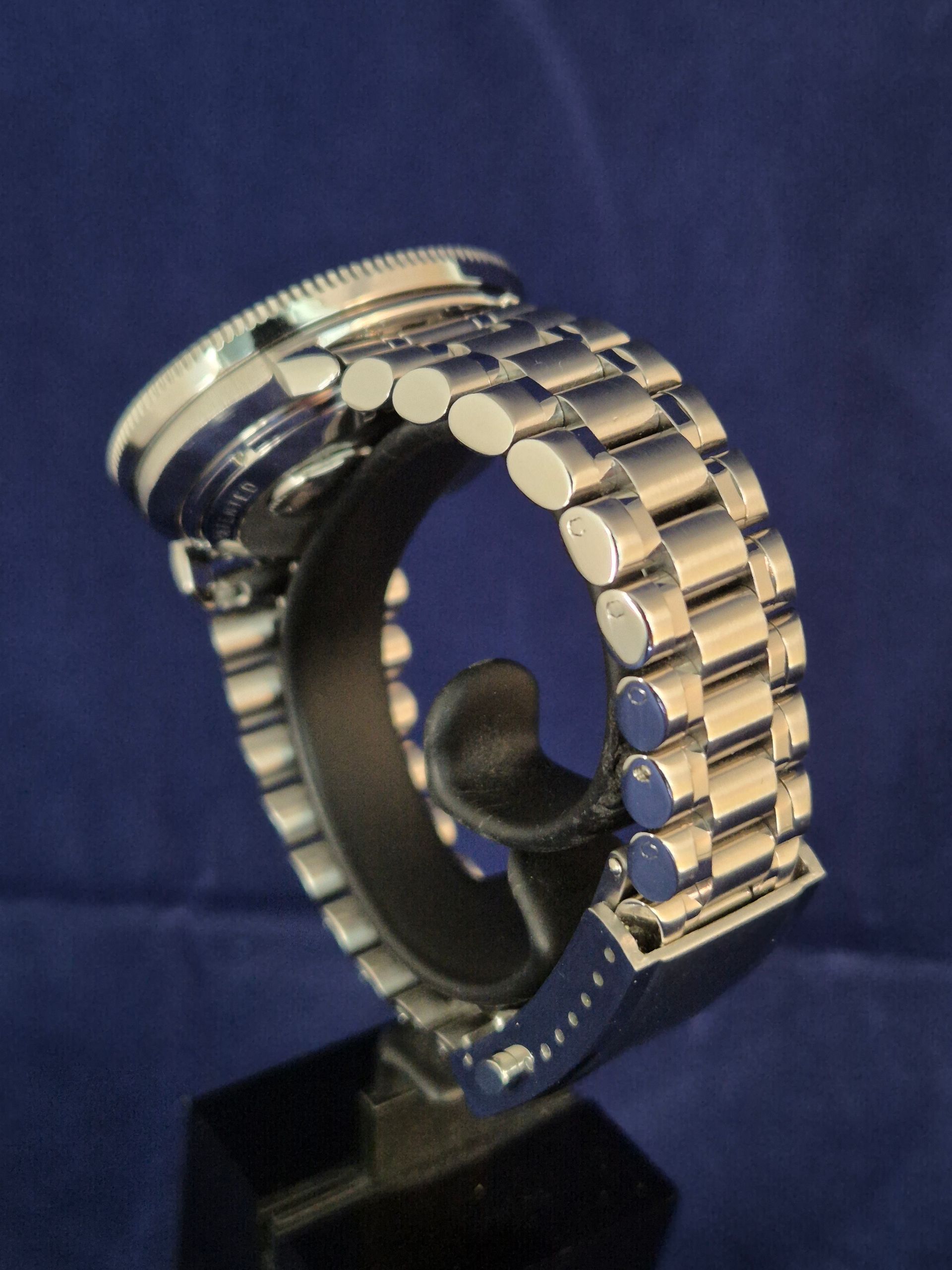 Silver metal wristwatch on a display stand against a dark blue background