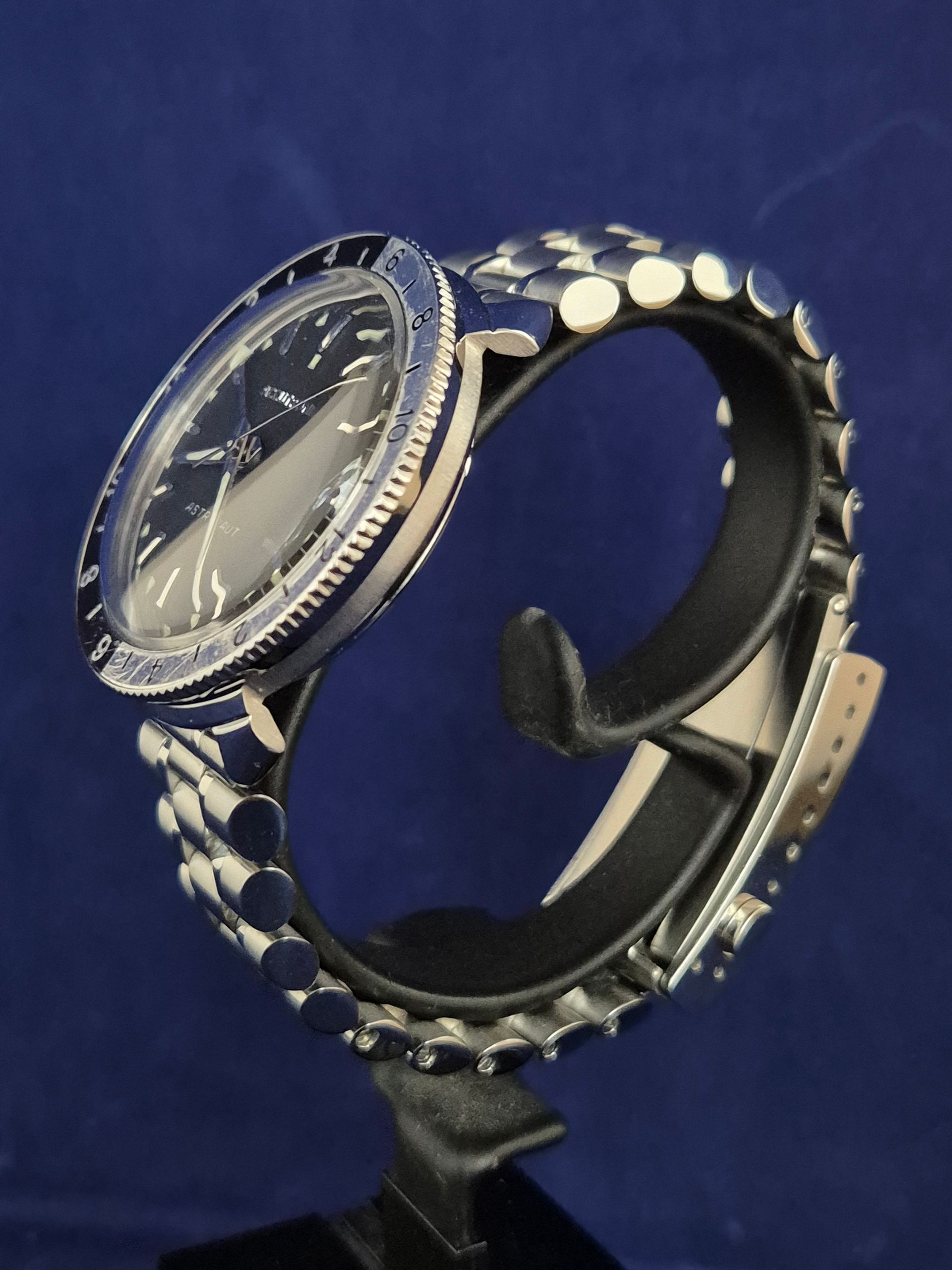 Black wristwatch with a studded band on a stand against a blue background