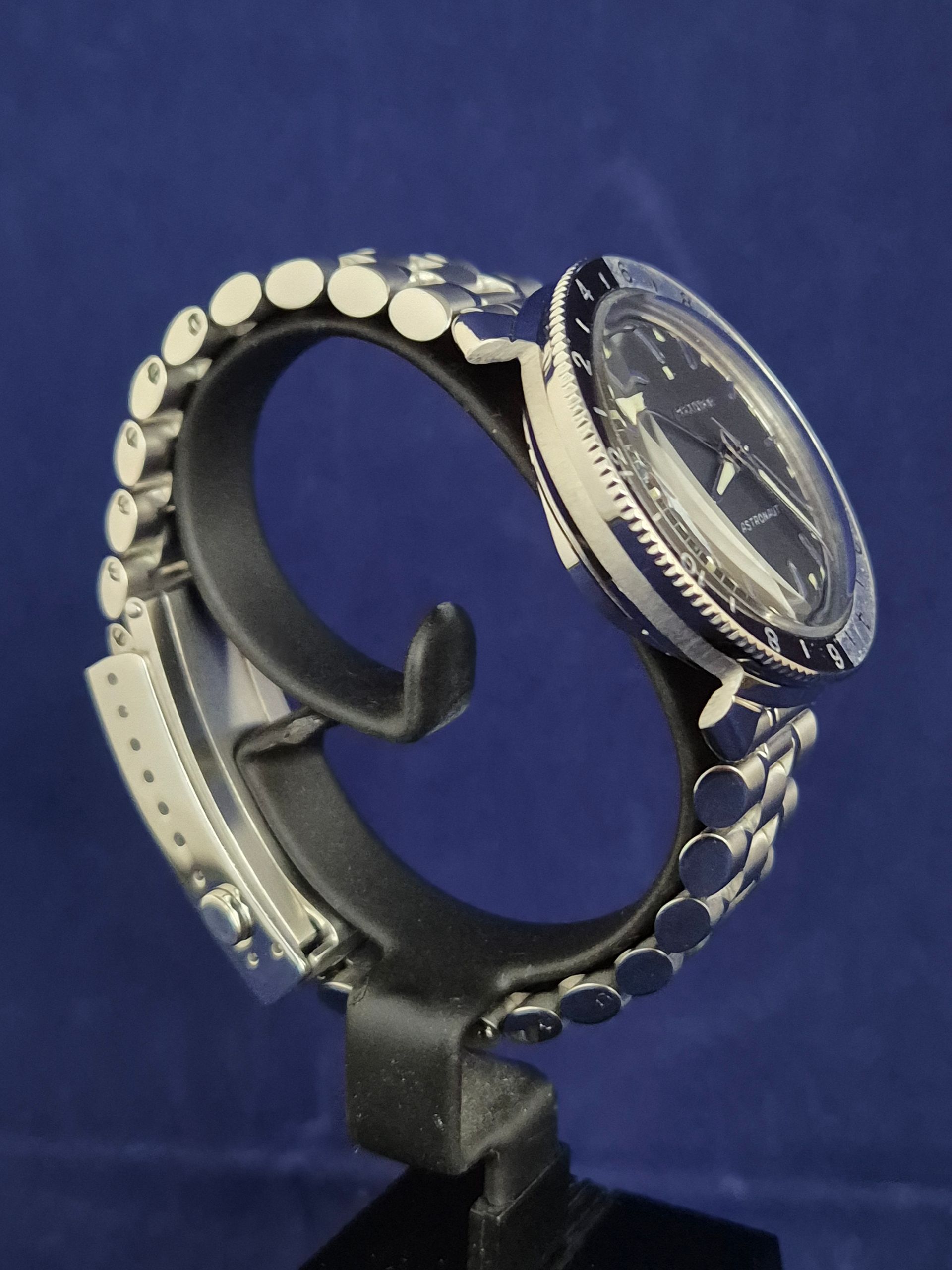 Silver wristwatch on a black stand against a blue background.