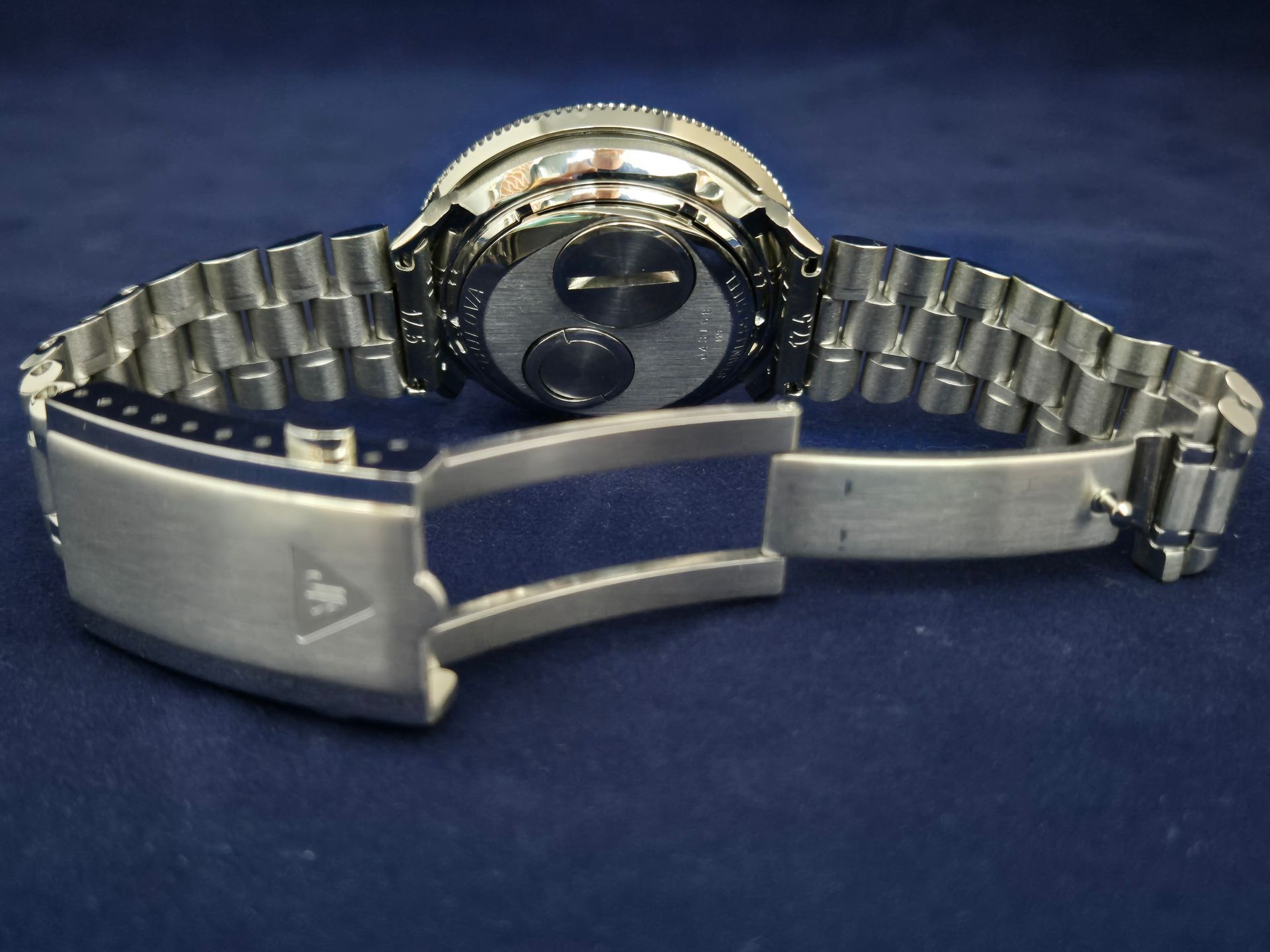 Close-up of a silver wristwatch with metal band and clasp, laid open on a blue surface