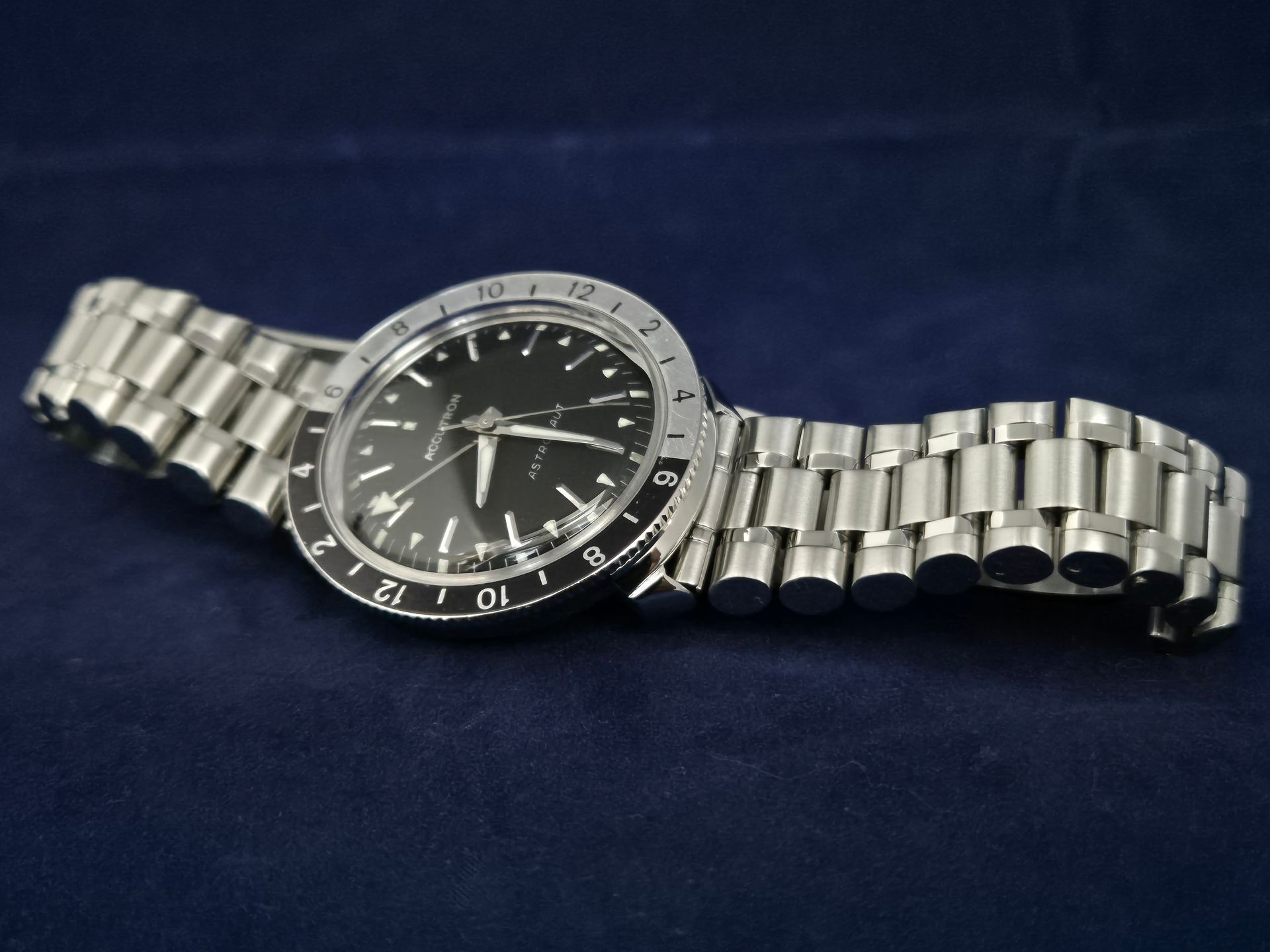 Silver wristwatch with black face and metal link band on a dark blue surface