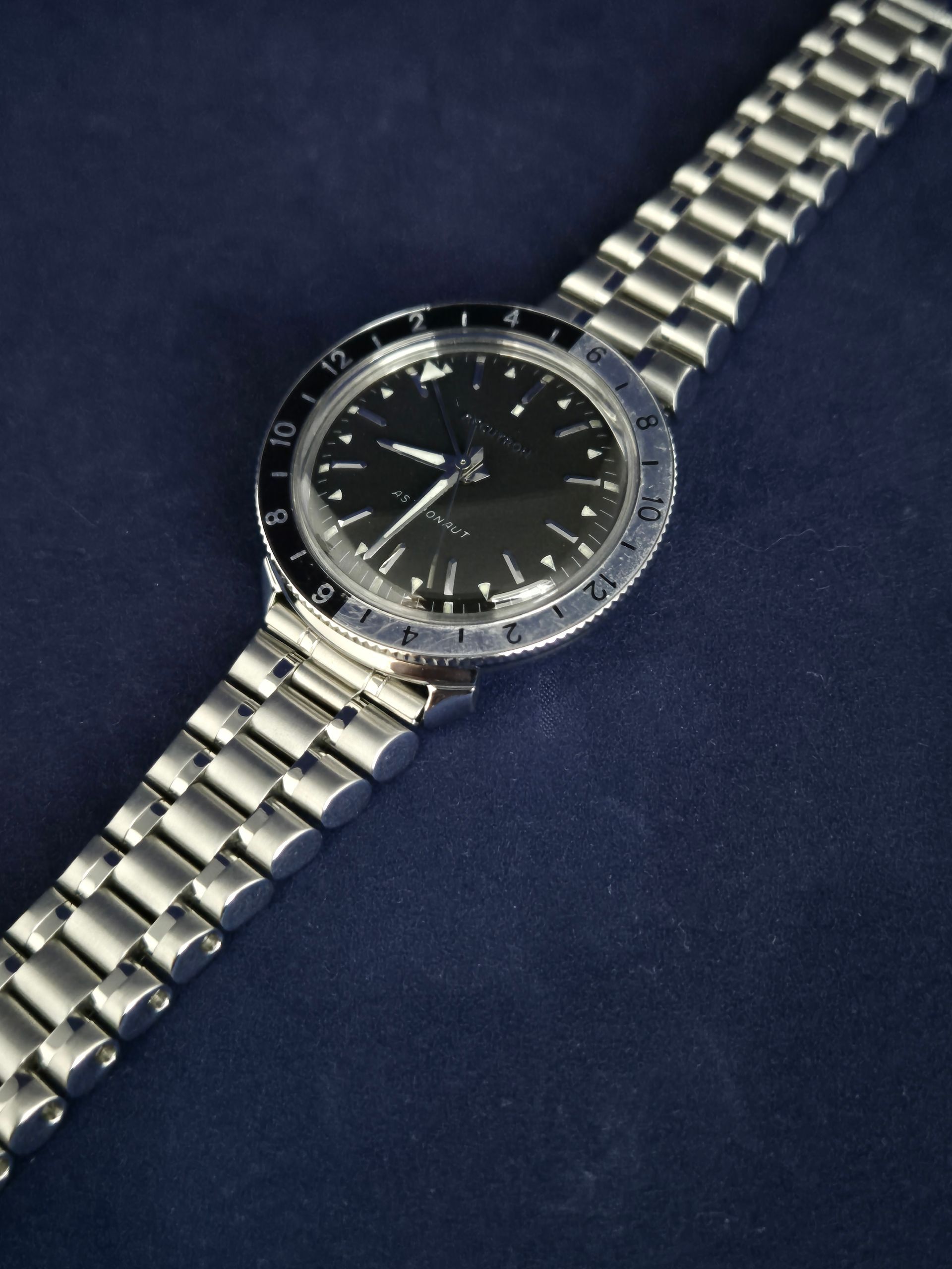 Silver wristwatch with black dial and metal bracelet on a dark blue background