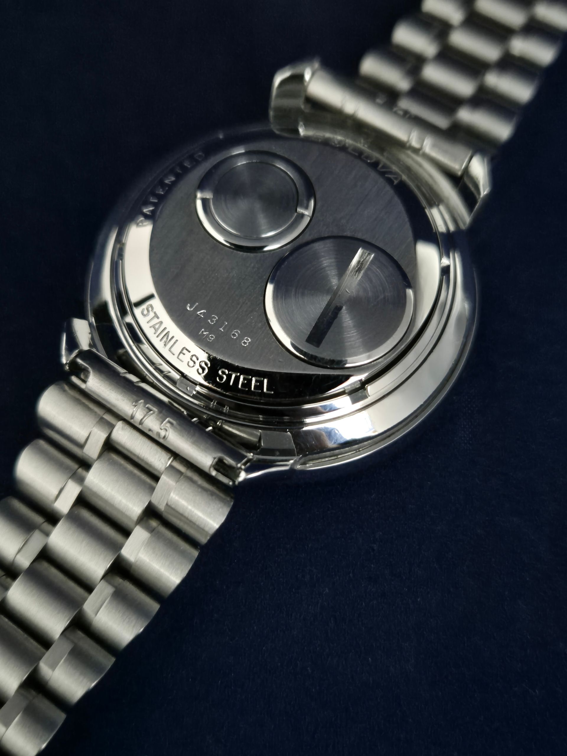 Close-up of a stainless steel wristwatch with two large buttons on a metal bracelet