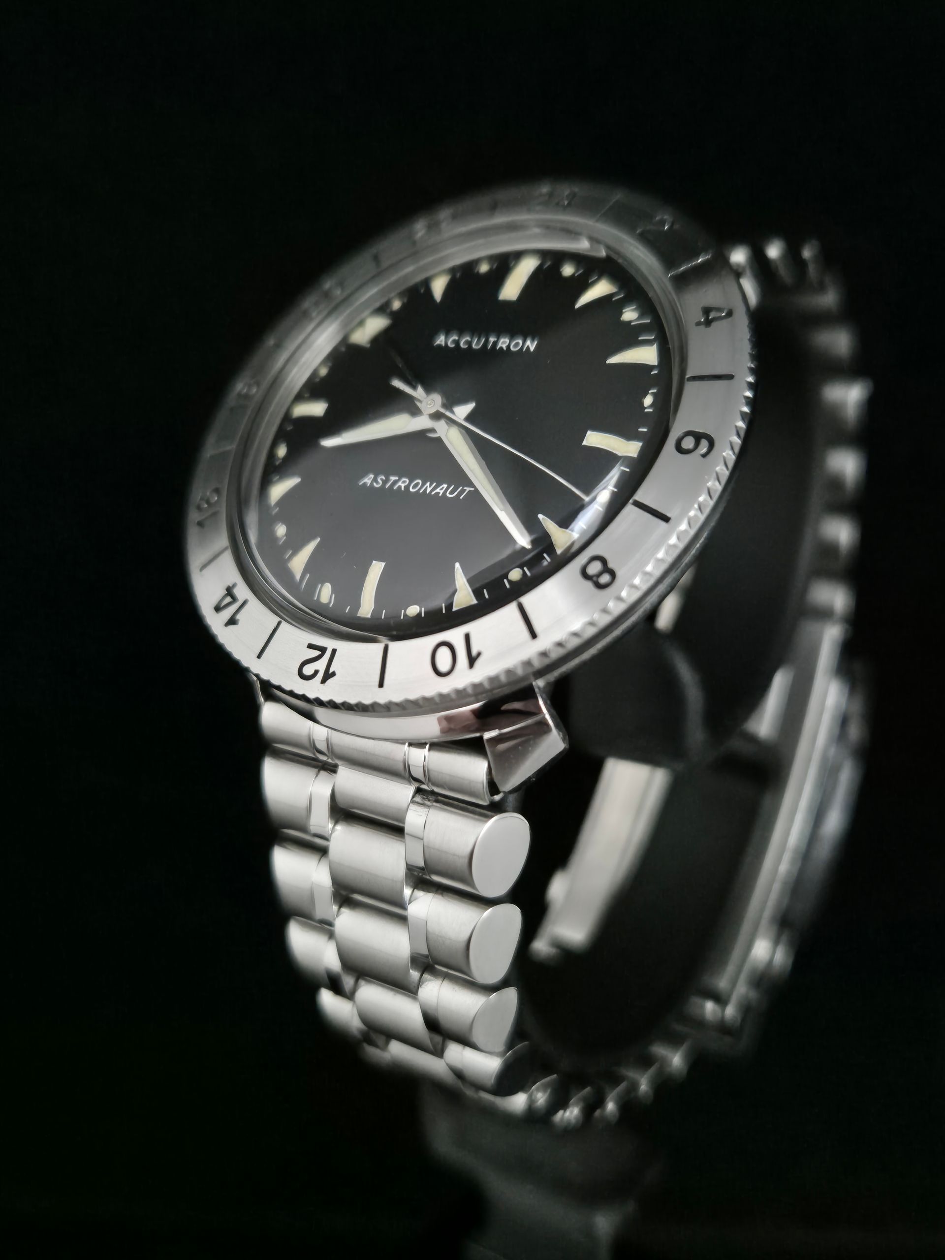 Silver-and-black wristwatch with a black dial and rotating bezel on a dark background