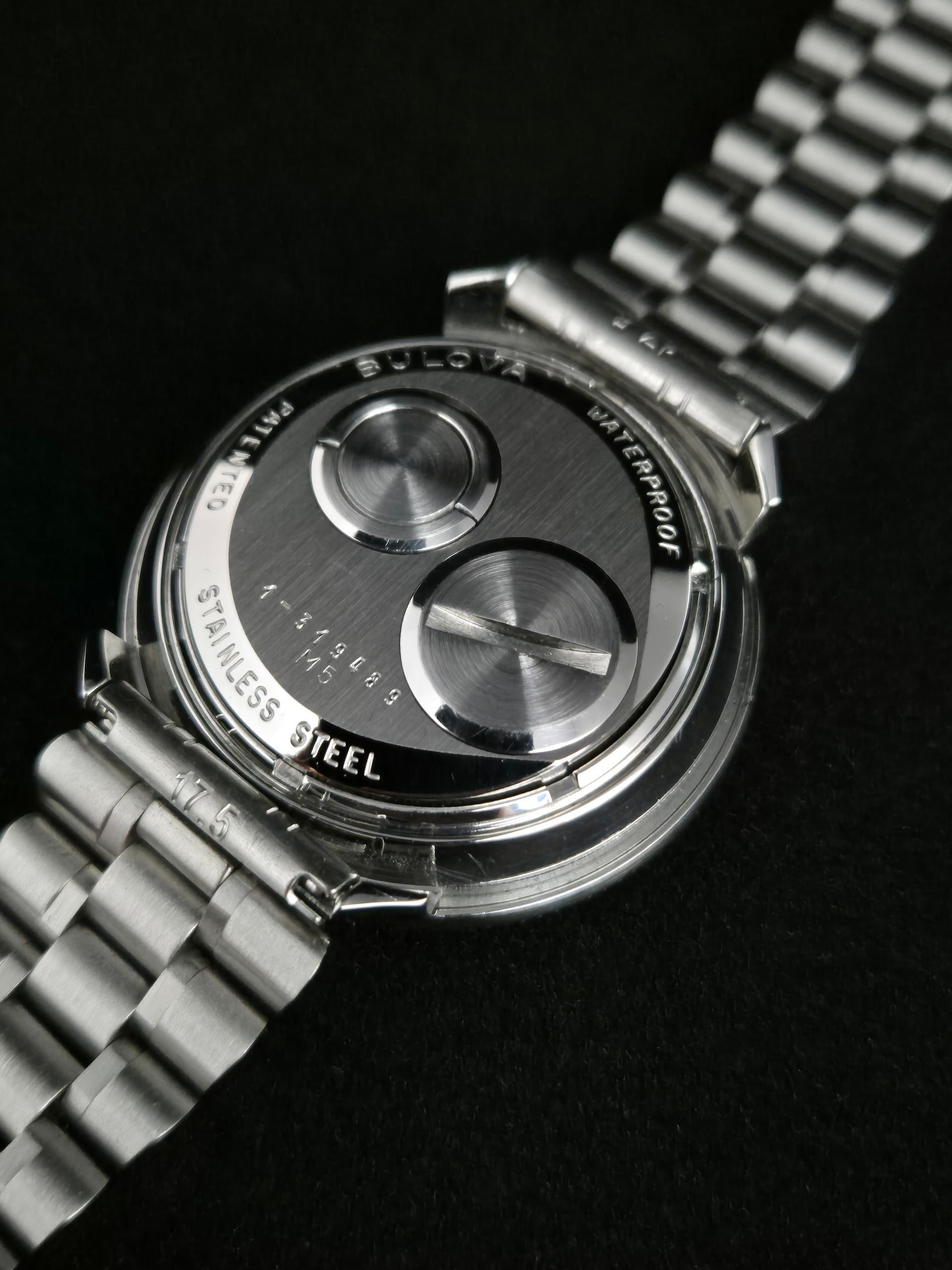 Close-up of a silver metal wristwatch with a black dial on a dark background