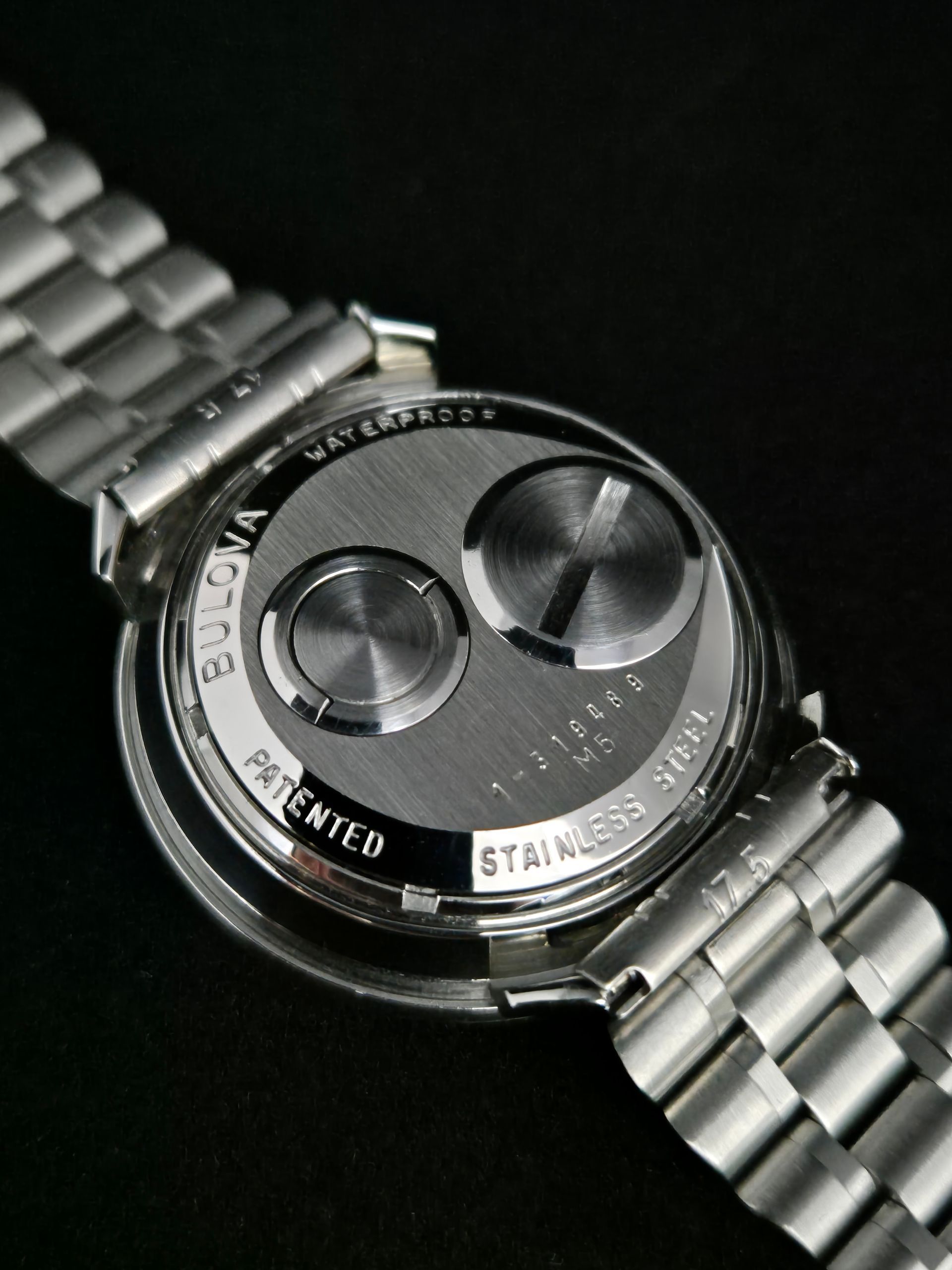 Close-up of a silver wristwatch with a stainless steel band and black face on a dark background