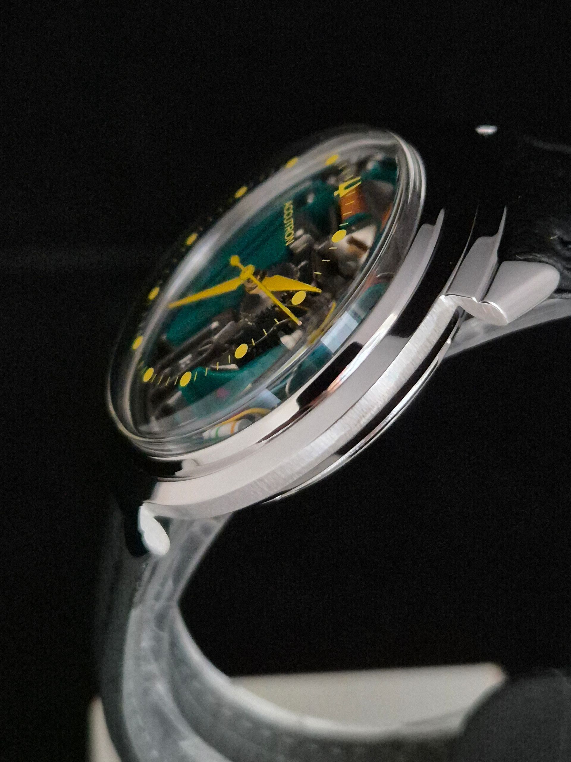 Transparent analog wristwatch with exposed green and yellow mechanics on a silver band against a black background