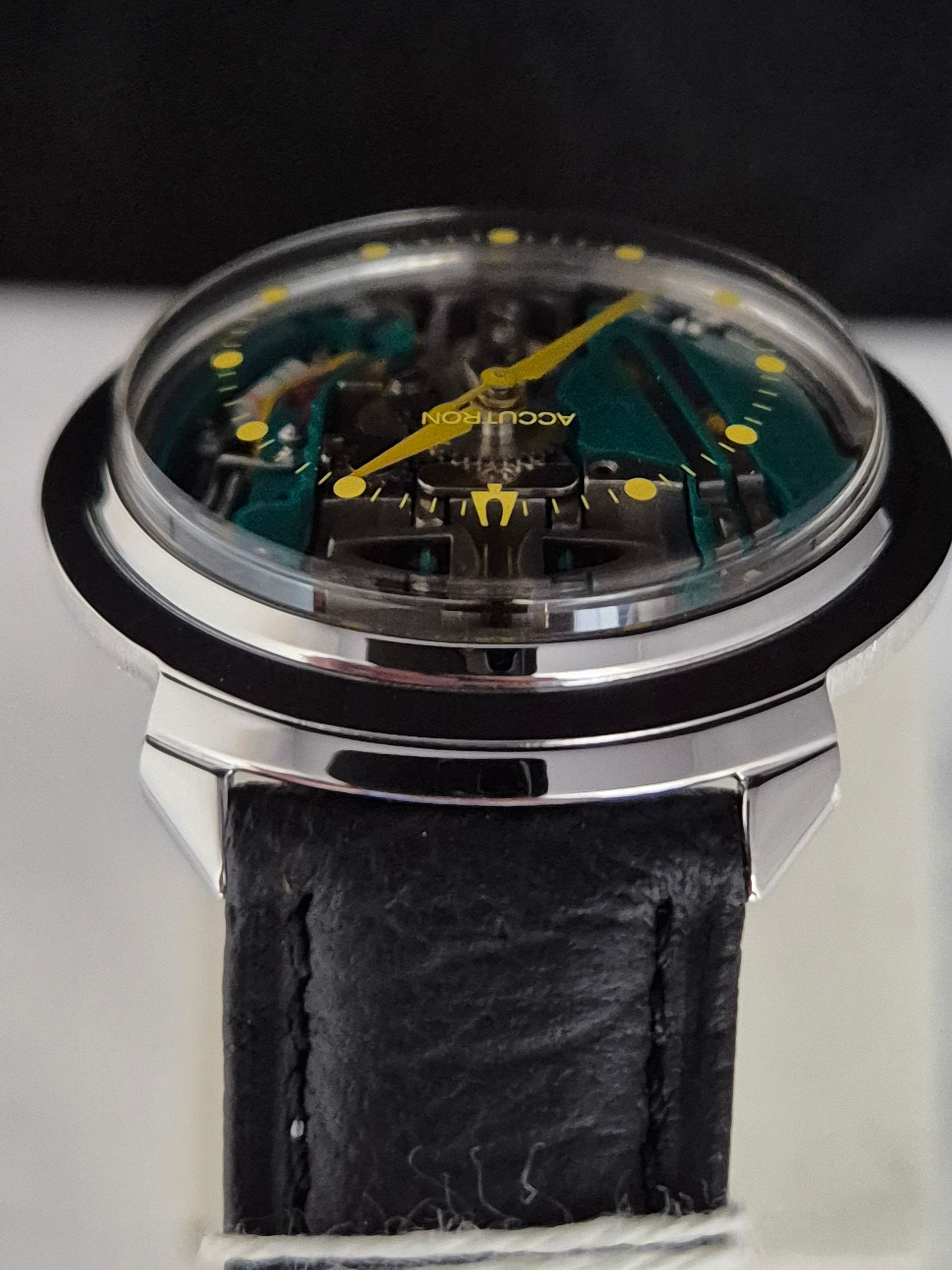 Close-up of a black leather watch strap and silver watch with a dark green dial