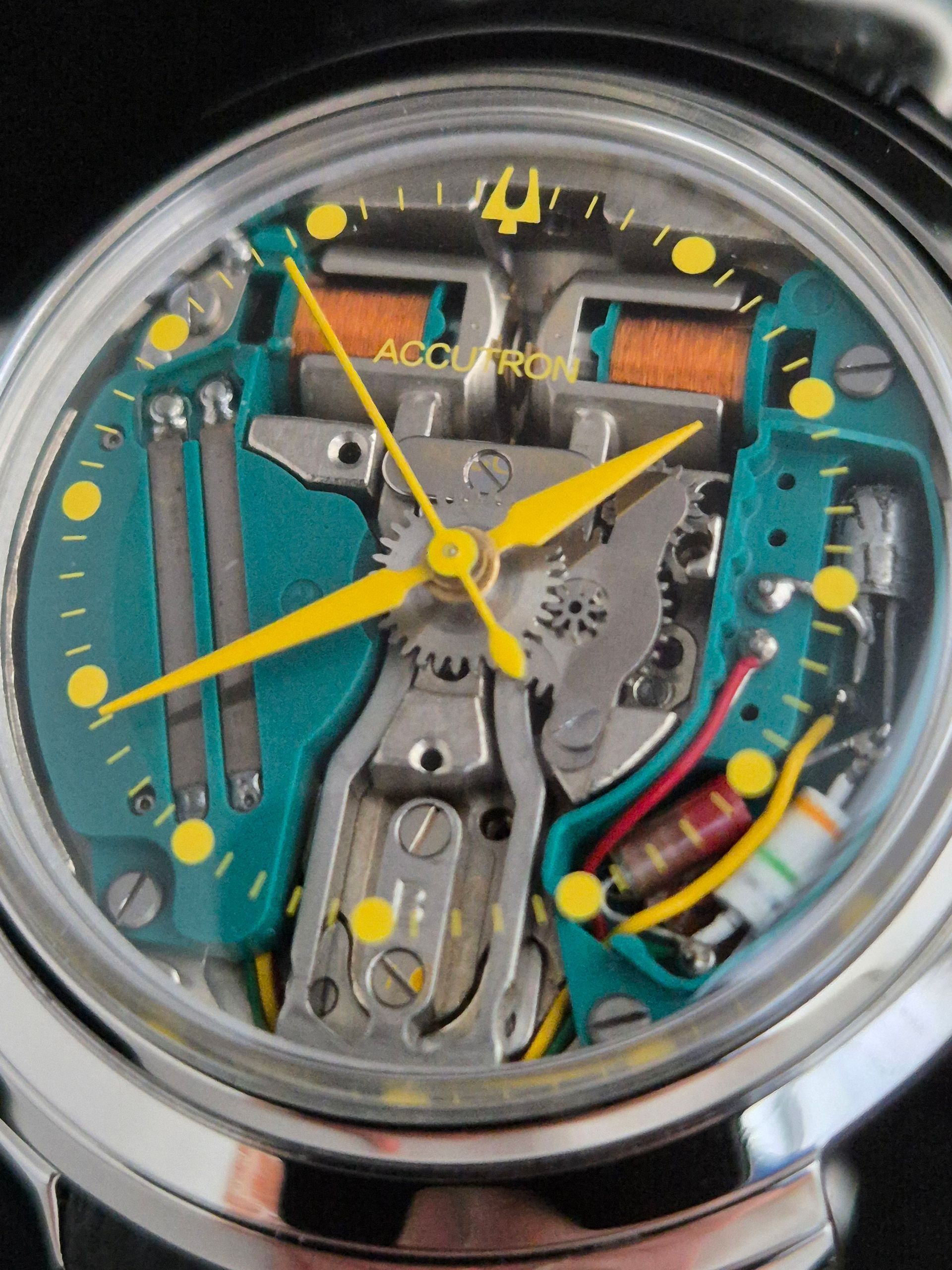 Close-up of a transparent watch face showing colorful exposed mechanical parts and yellow hands