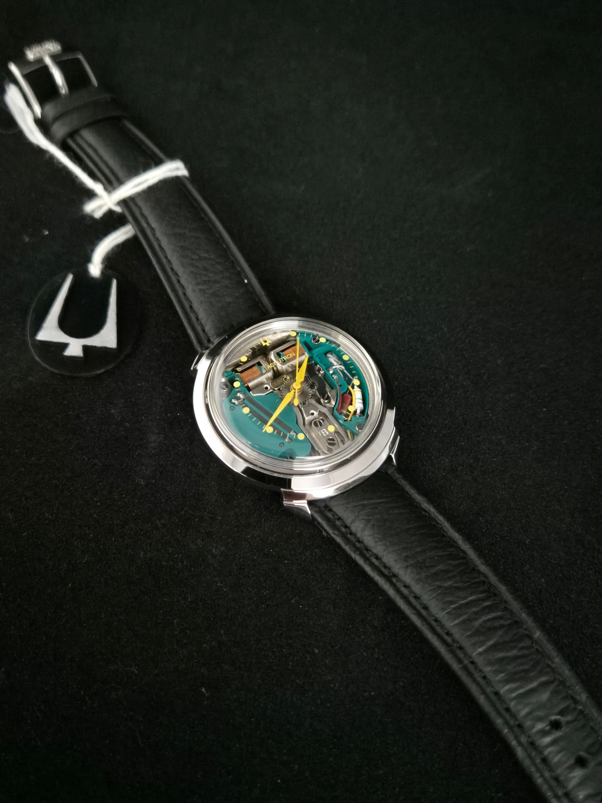 Luxury wristwatch with black leather strap and visible mechanical movement on a dark background