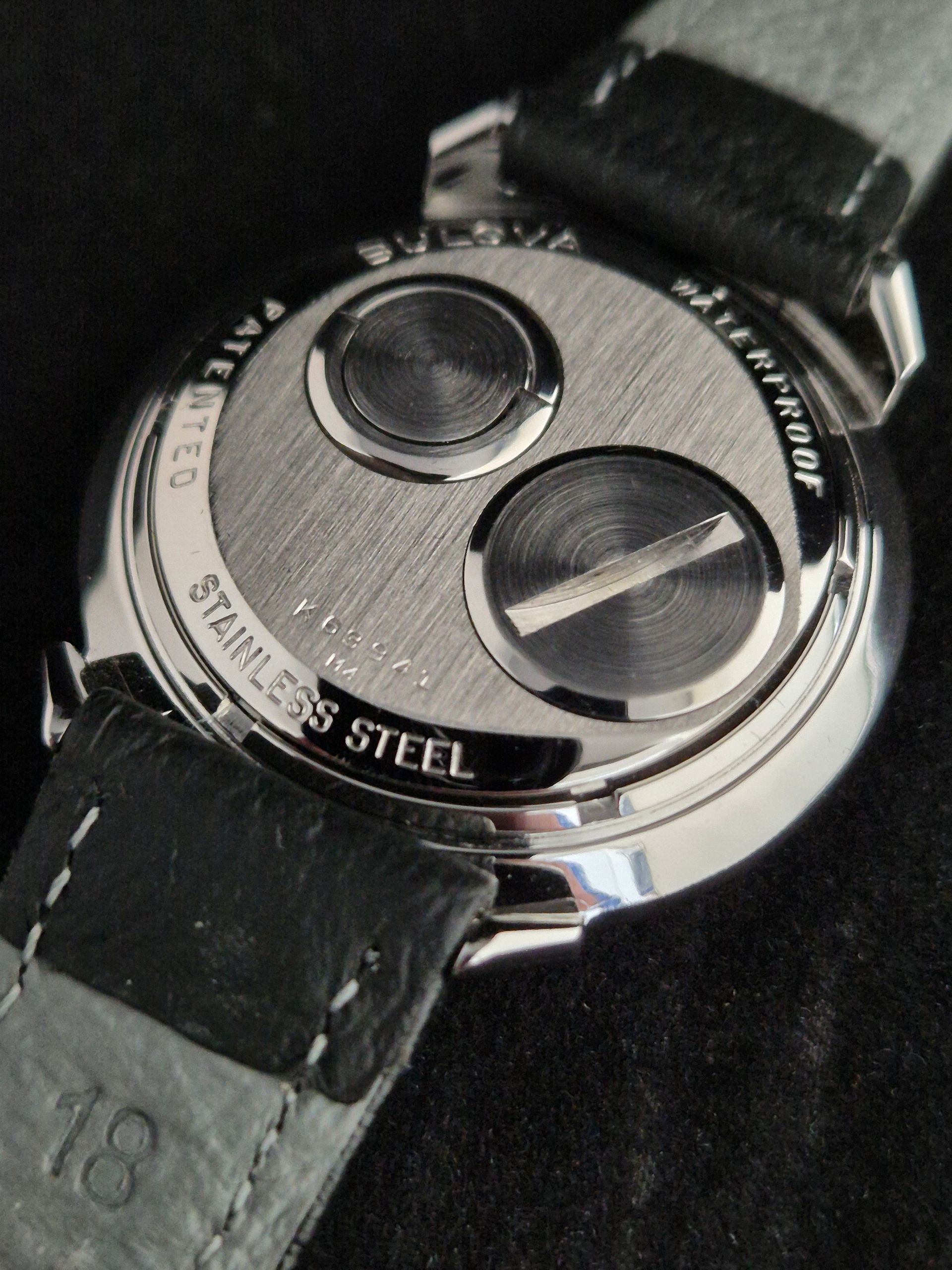 Close-up of a silver stainless steel wristwatch with a black leather strap on a dark background