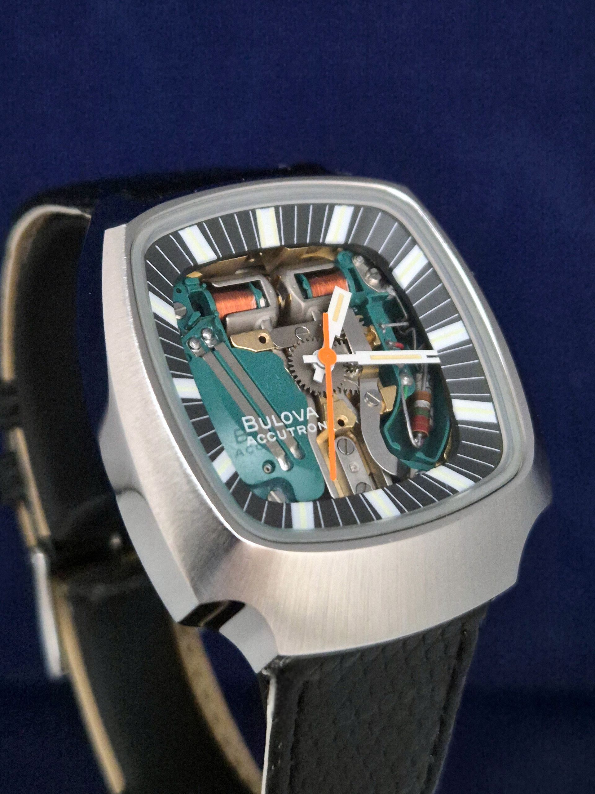 Close-up of a silver Bulova wristwatch with a skeleton dial and black leather strap on a blue background