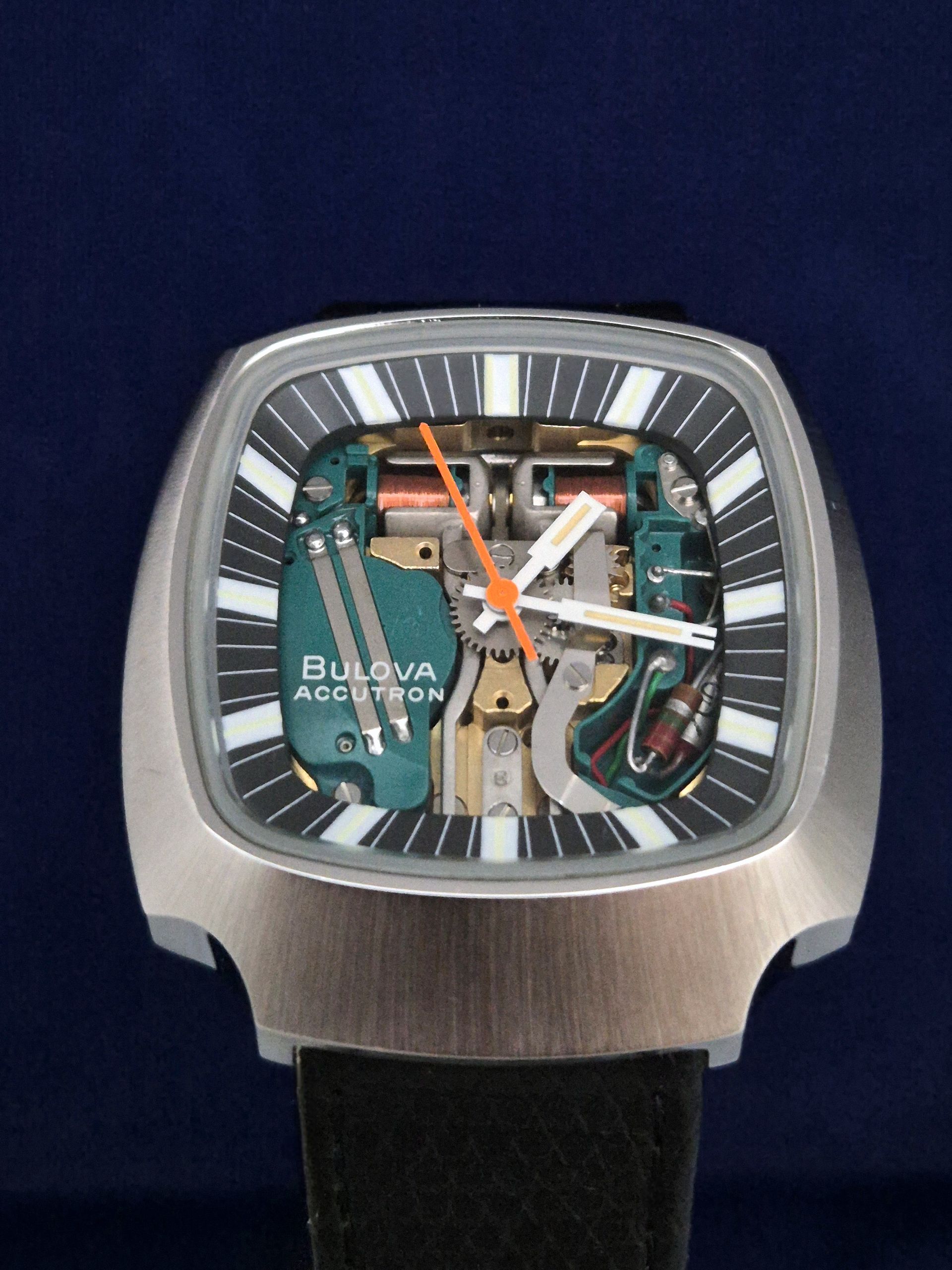 Bulova wristwatch with transparent skeleton dial, silver square case, and black strap on dark blue background