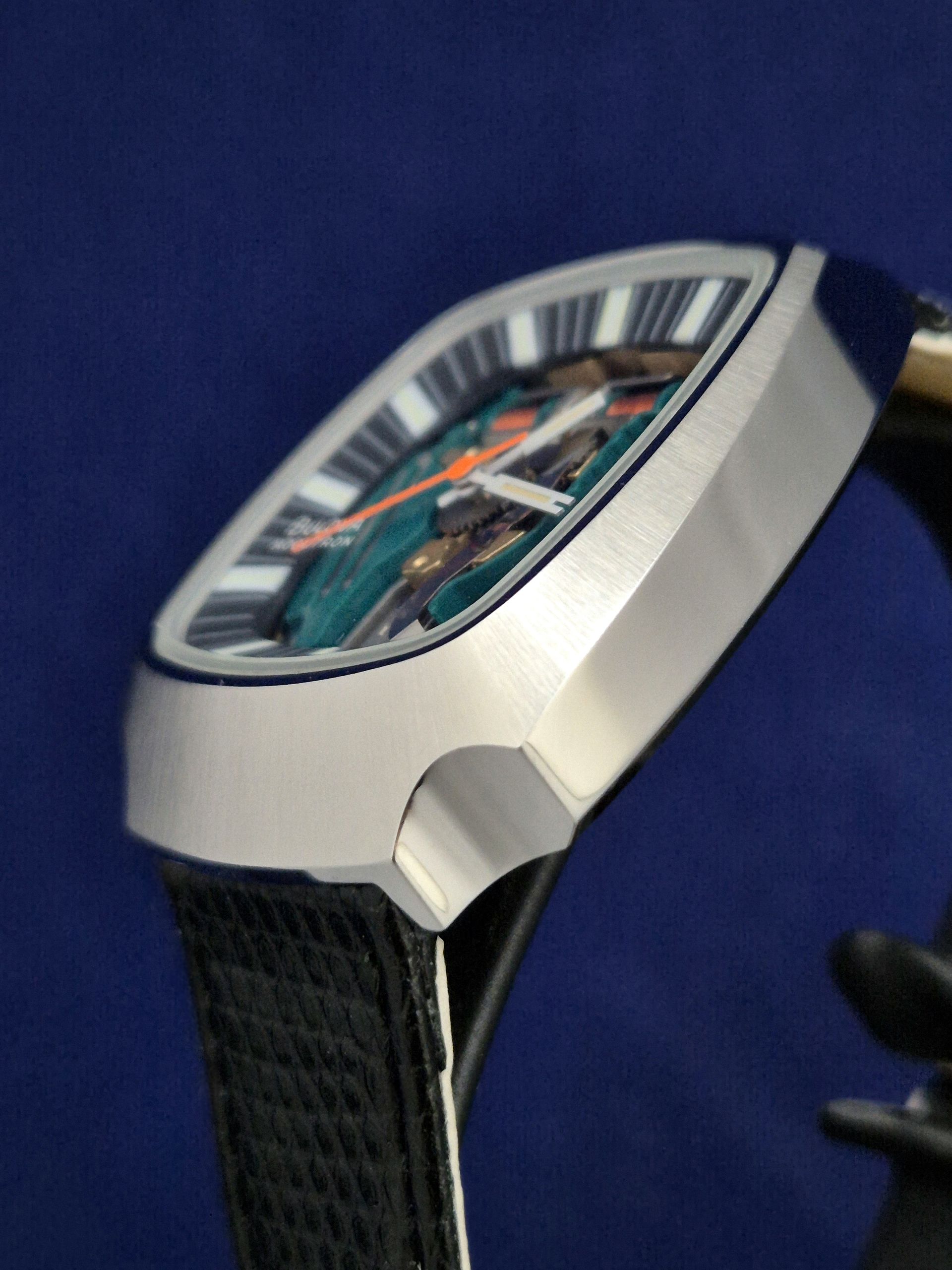 Close-up of a silver wristwatch with a black strap and visible mechanical movement on a blue background
