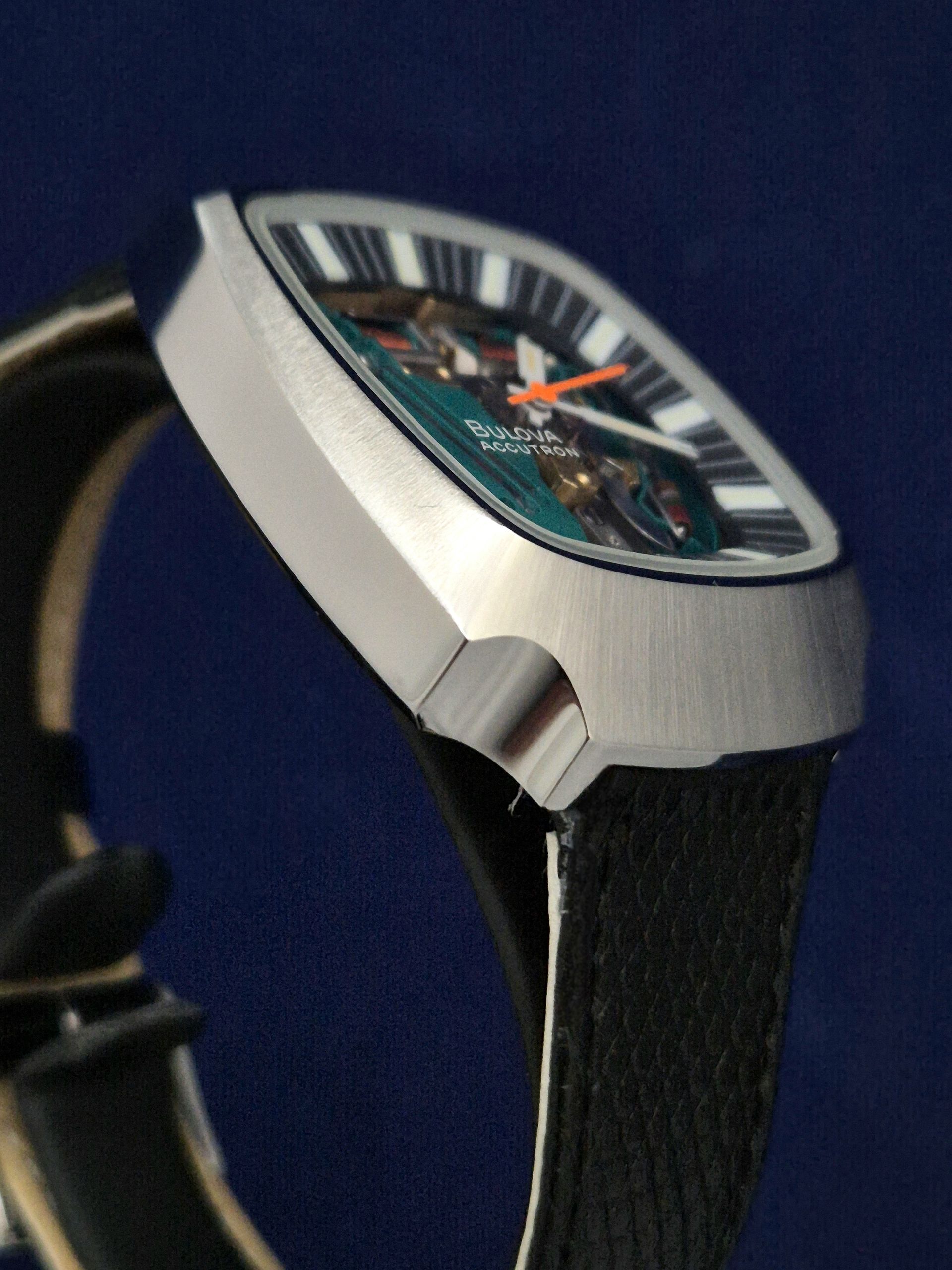 Close-up of a silver wristwatch with a black strap and teal dial on a dark blue background
