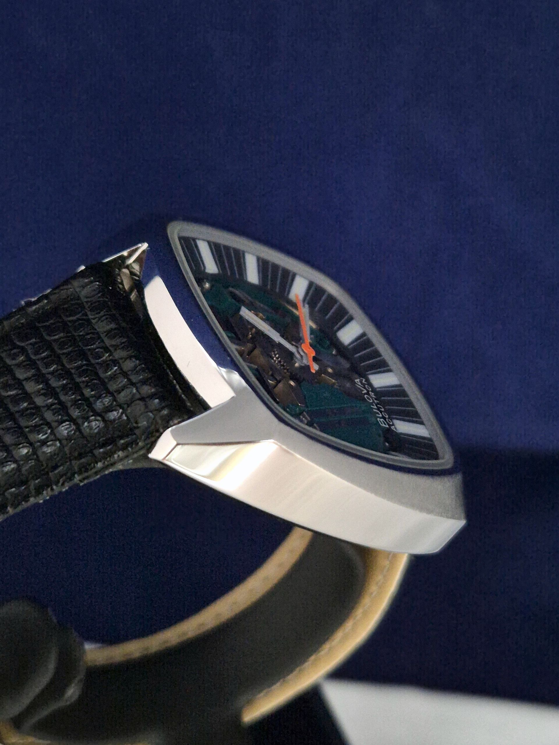 Close-up of a silver wristwatch with a black dial and black leather strap on a dark blue background