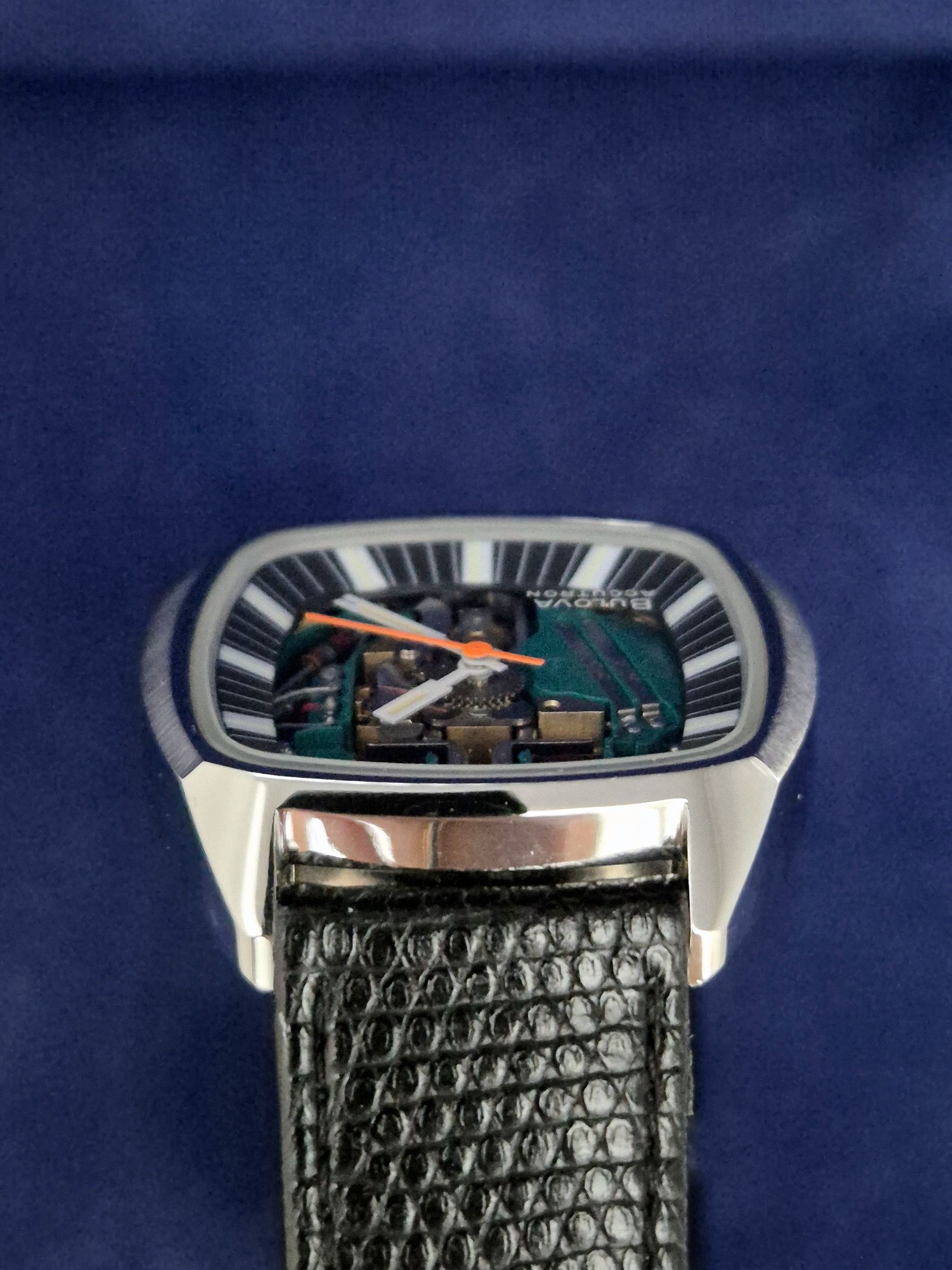 Close-up of a silver watch with a striped rectangular face and dark textured leather strap.