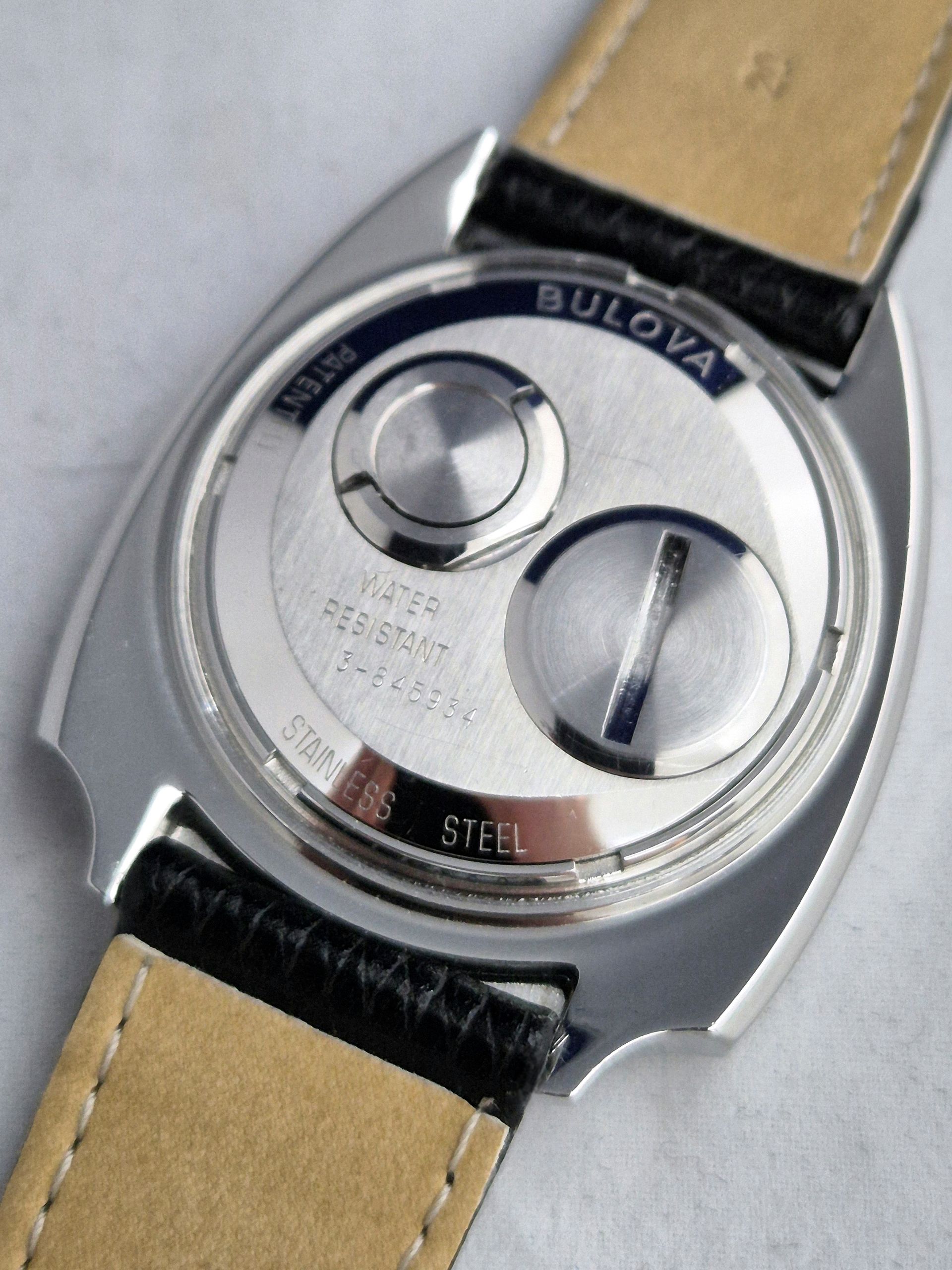 Close-up of a Bulova watch back with two circular compartments on a beige leather strap.