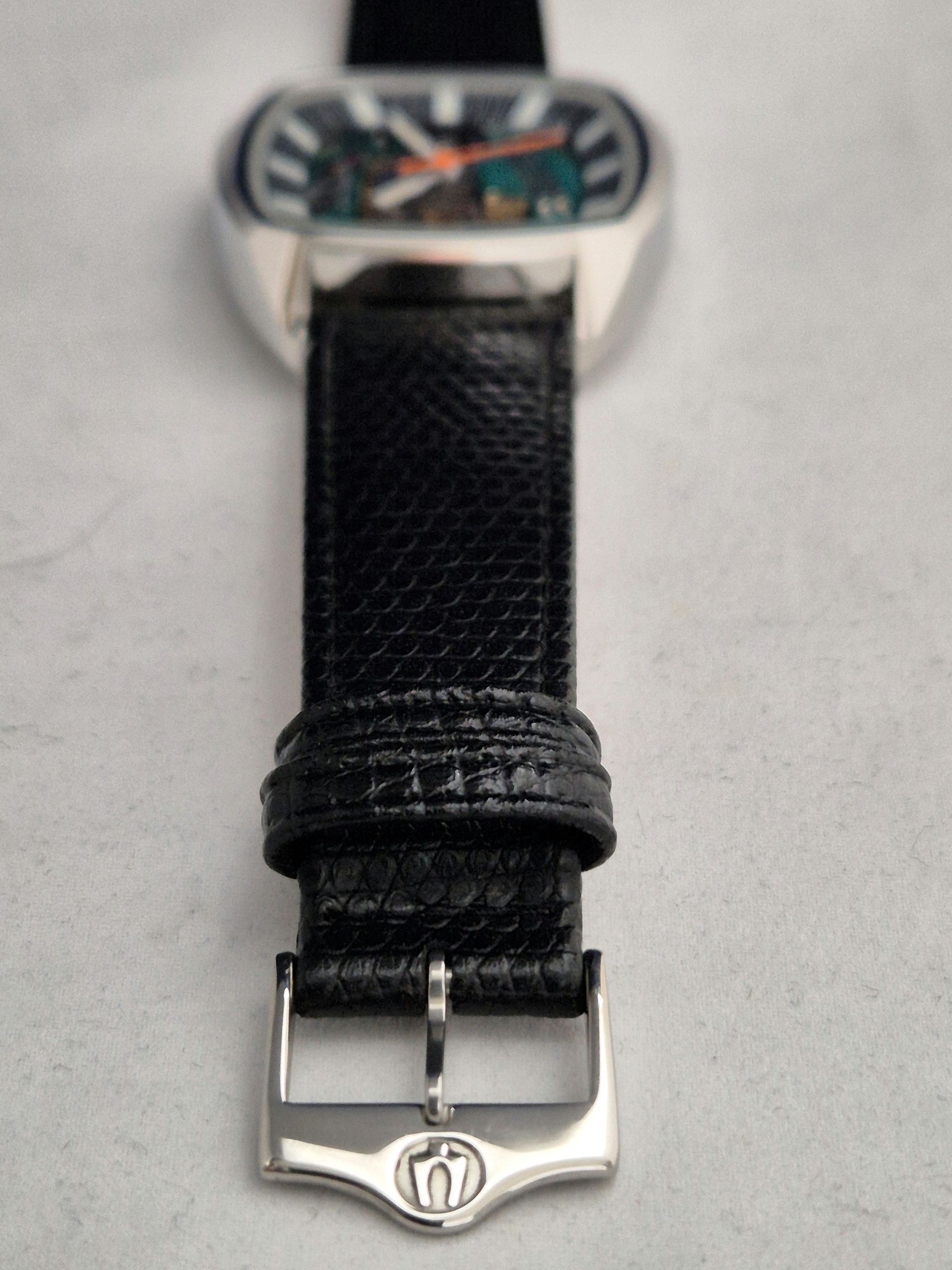 Close-up of a black watch strap and silver buckle beneath a blurred watch face.