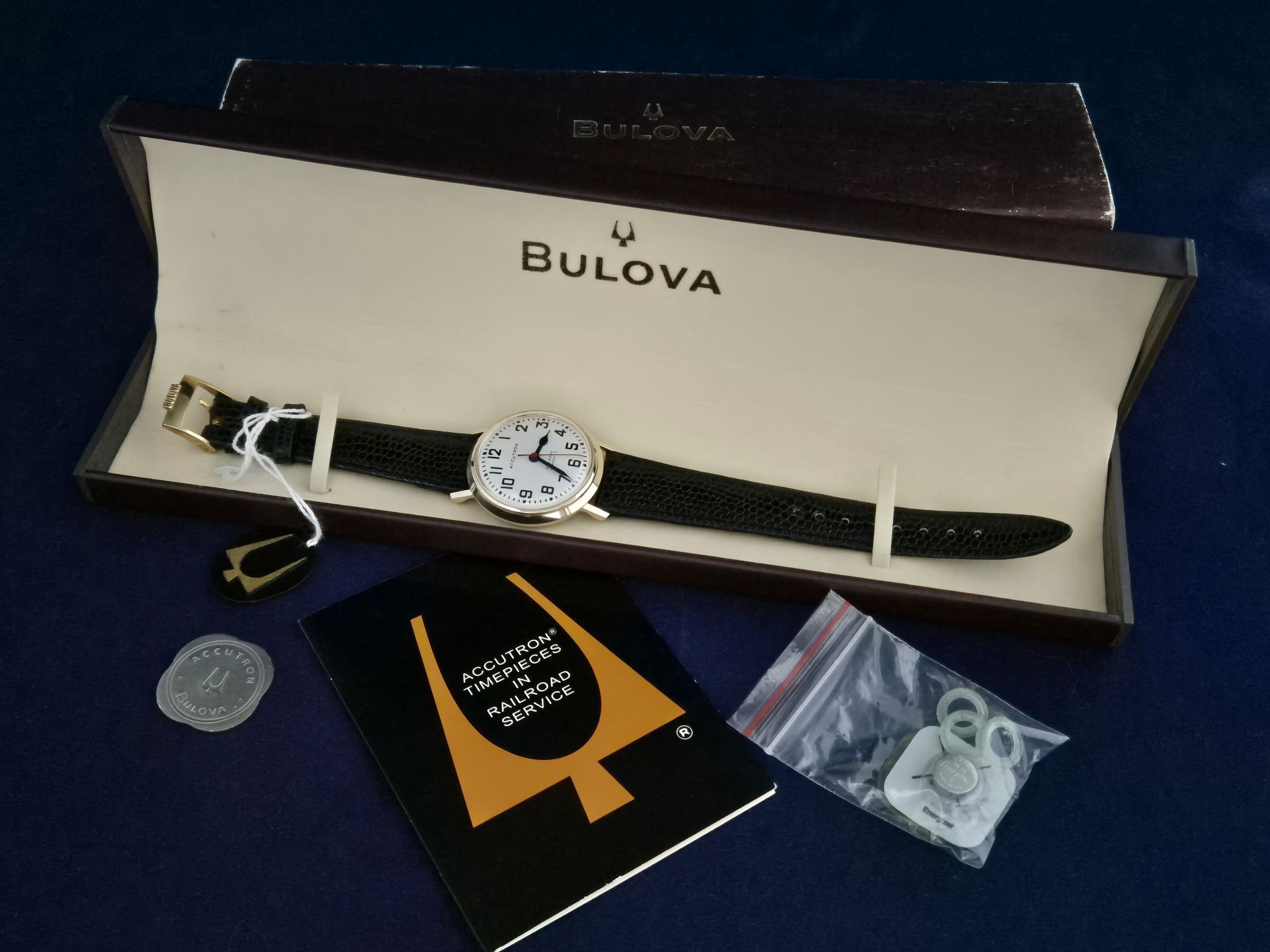 Bulova wristwatch set in open box with strap, warranty card, and accessories on a dark surface