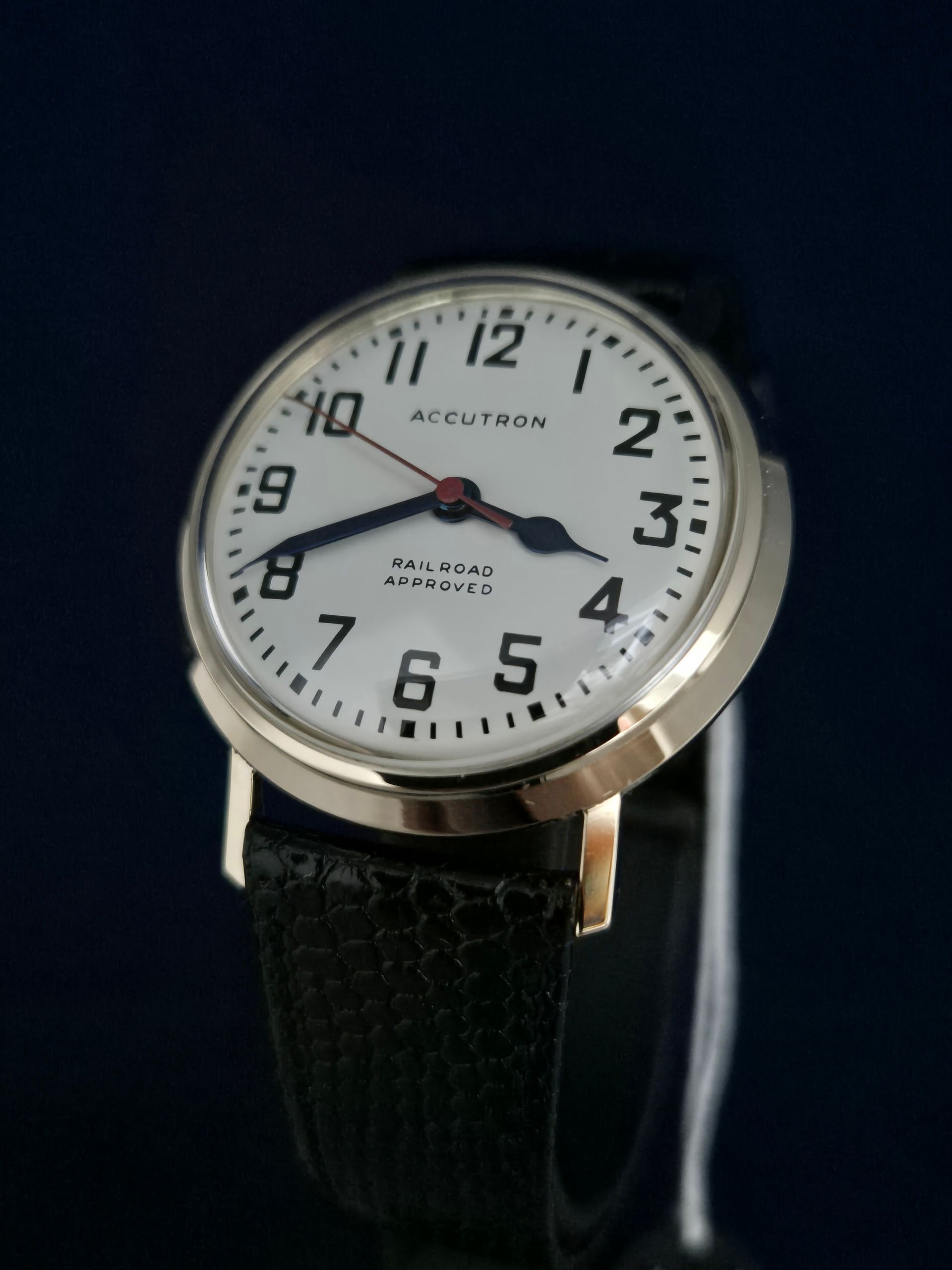 Close-up of a silver wristwatch with a white dial and black leather strap on a dark background