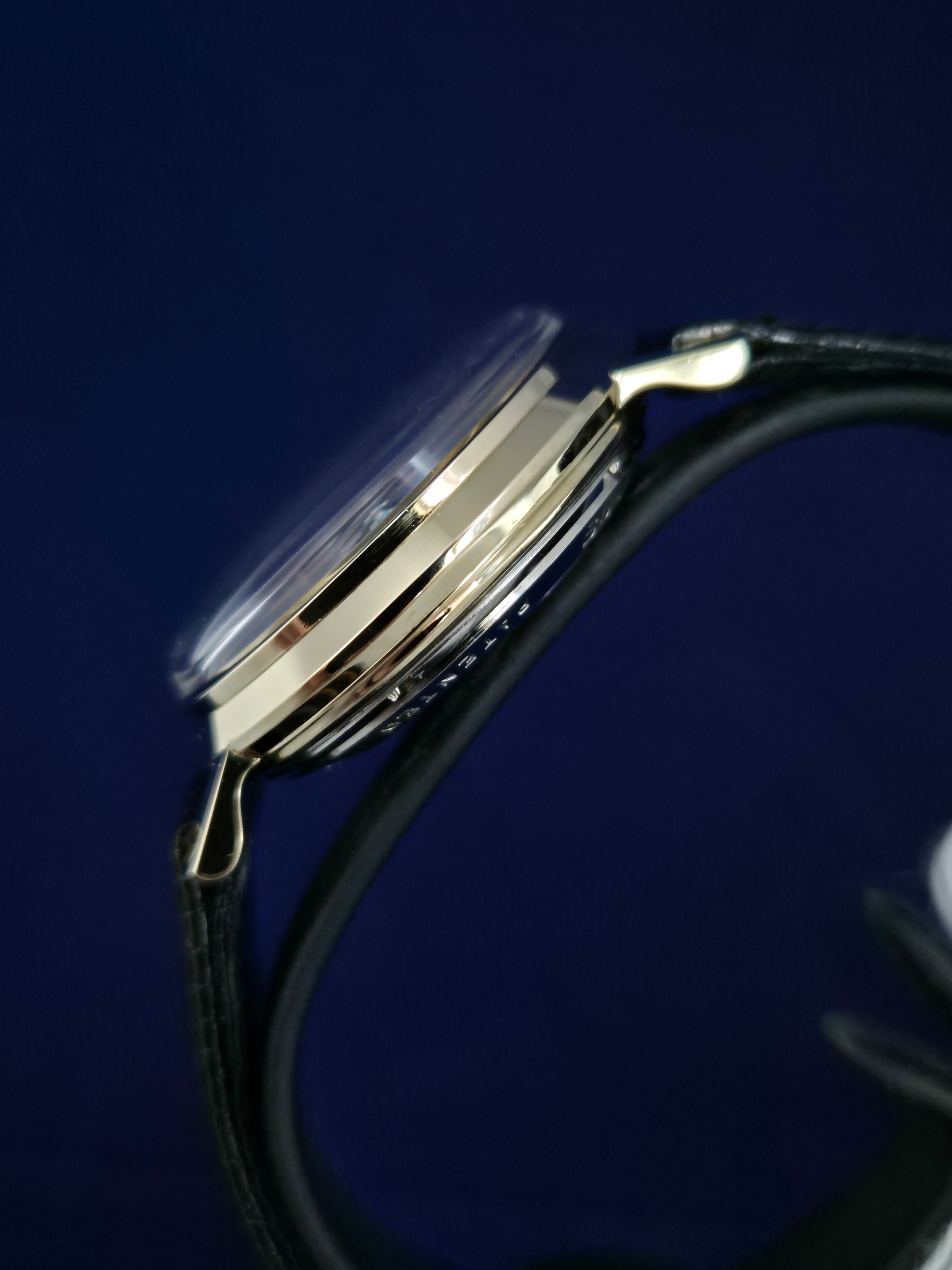 Close-up of a silver wristwatch on a black strap against a dark blue background