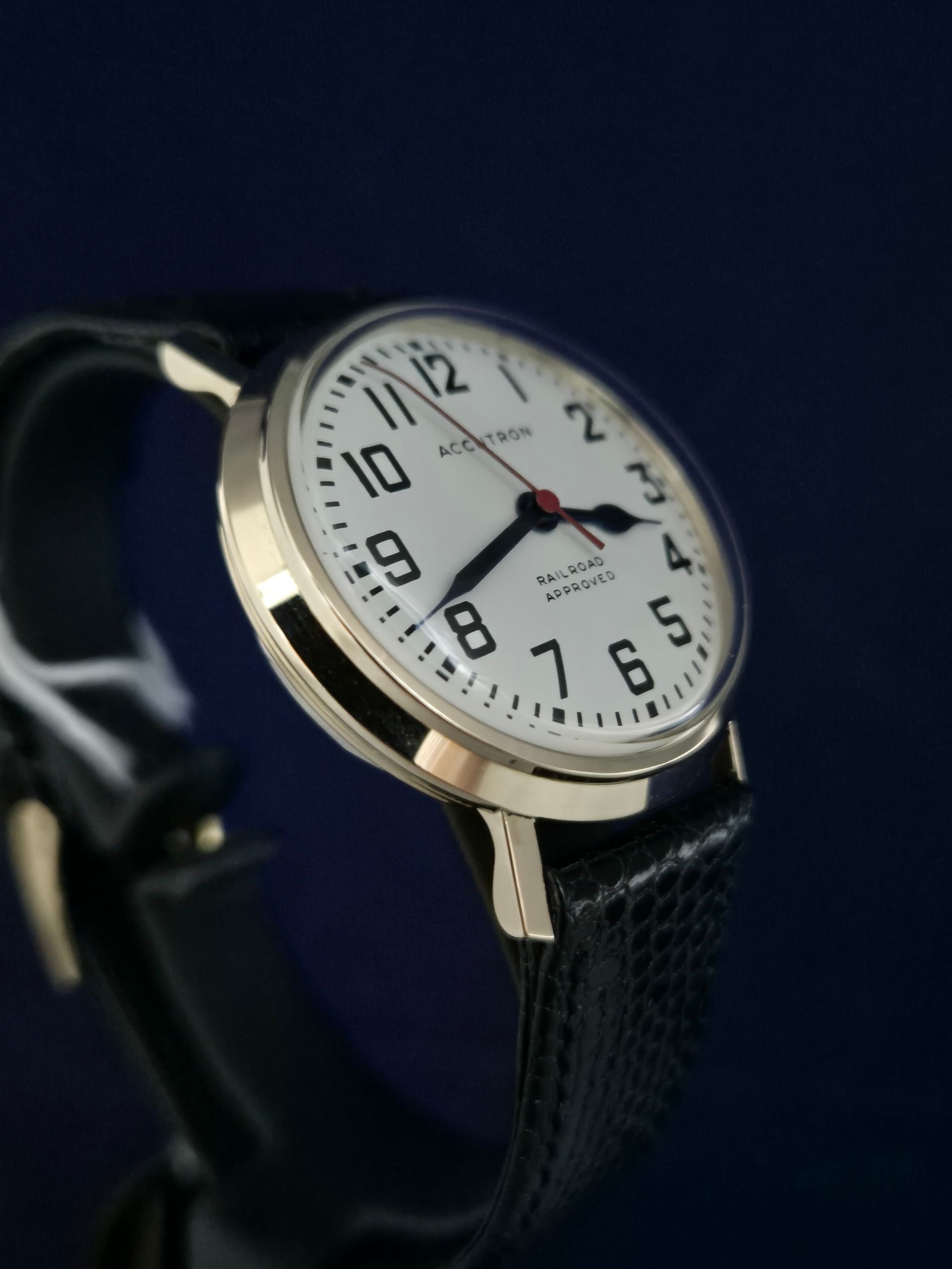 Silver wristwatch with white dial and black strap on a dark blue background