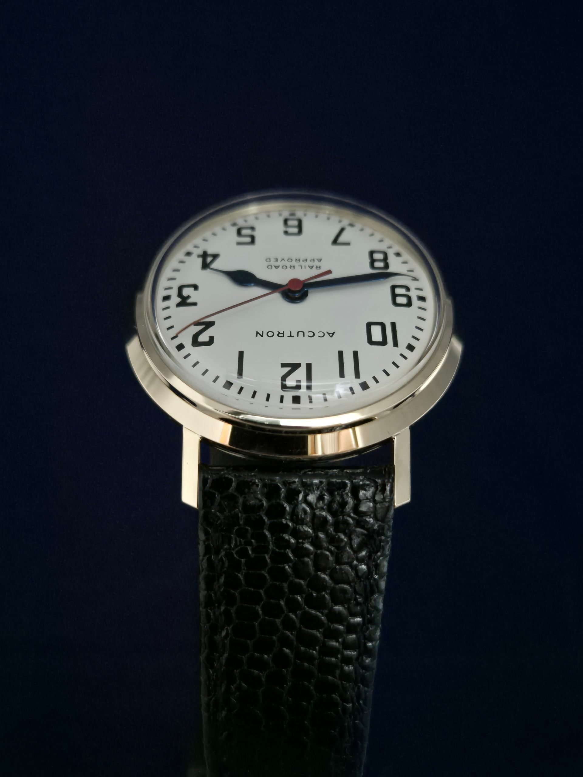 White-faced wristwatch with black leather strap on a dark background