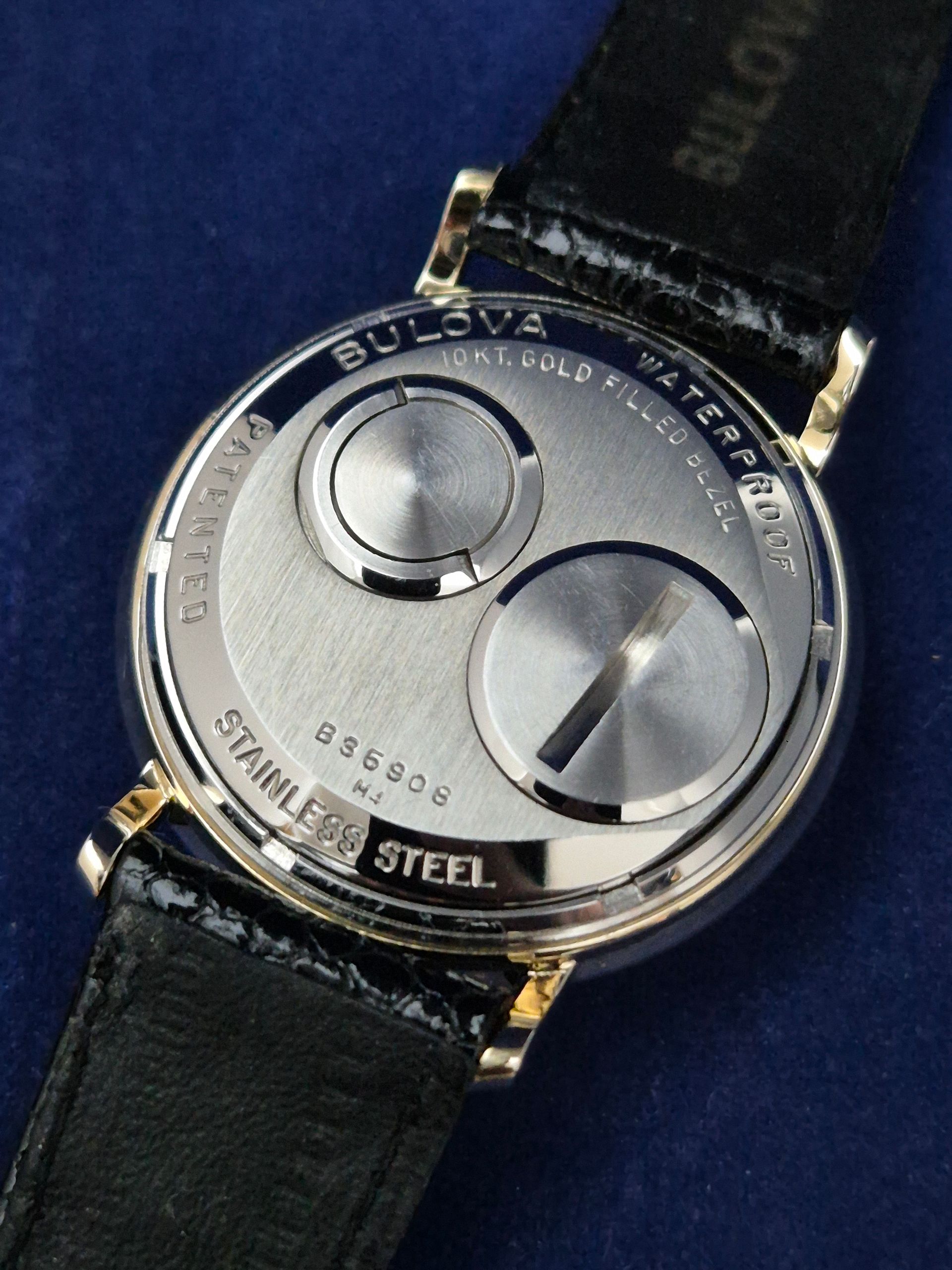 Back of a silver Bulova wristwatch with black leather strap on a blue background