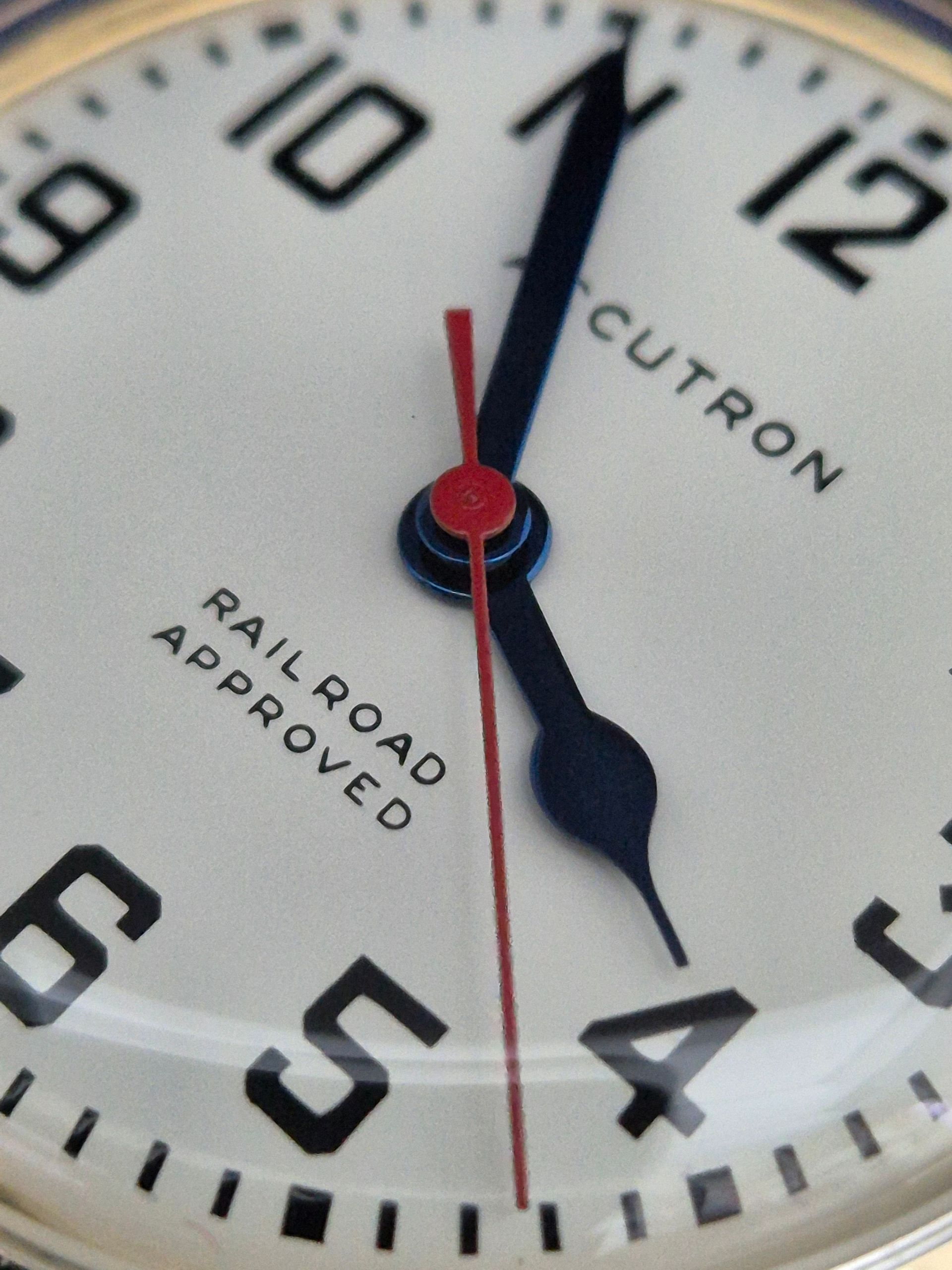 Close-up of a white clock face with black numerals and a red second hand, showing 12:24.