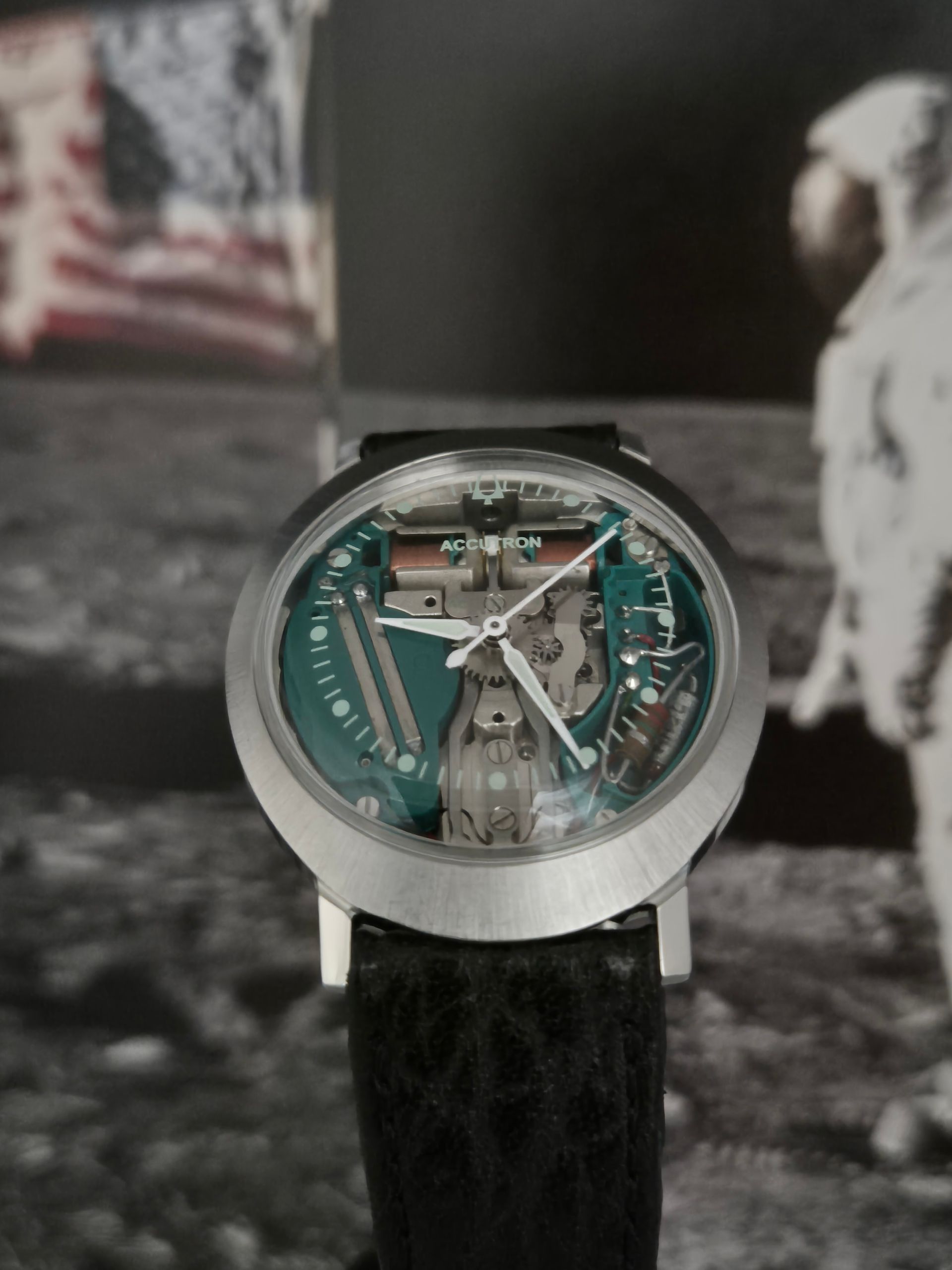 Close-up of a wristwatch with a silver case and black strap against a moon-landing background