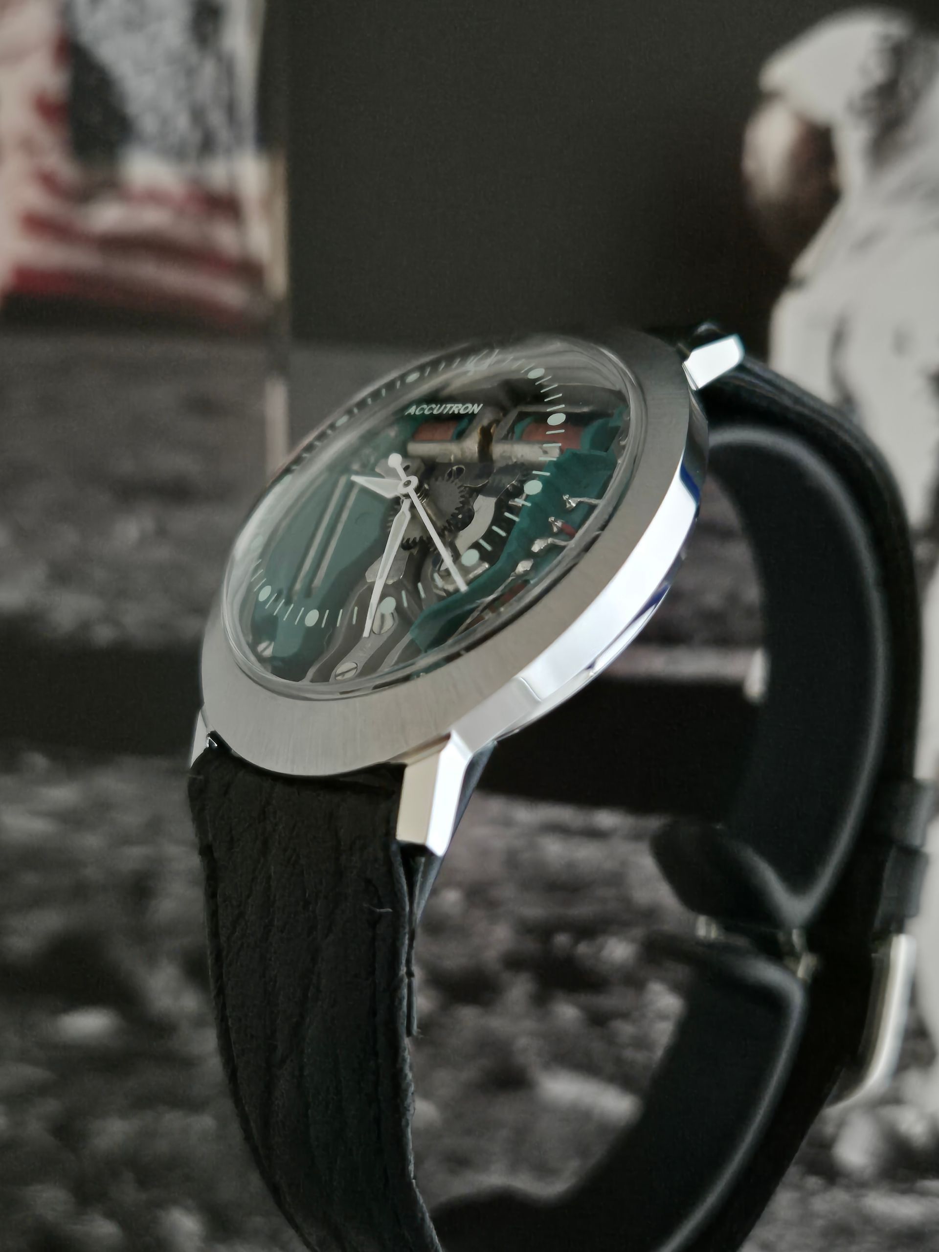 Close-up of a silver wristwatch with a black leather strap on a blurred grayscale background
