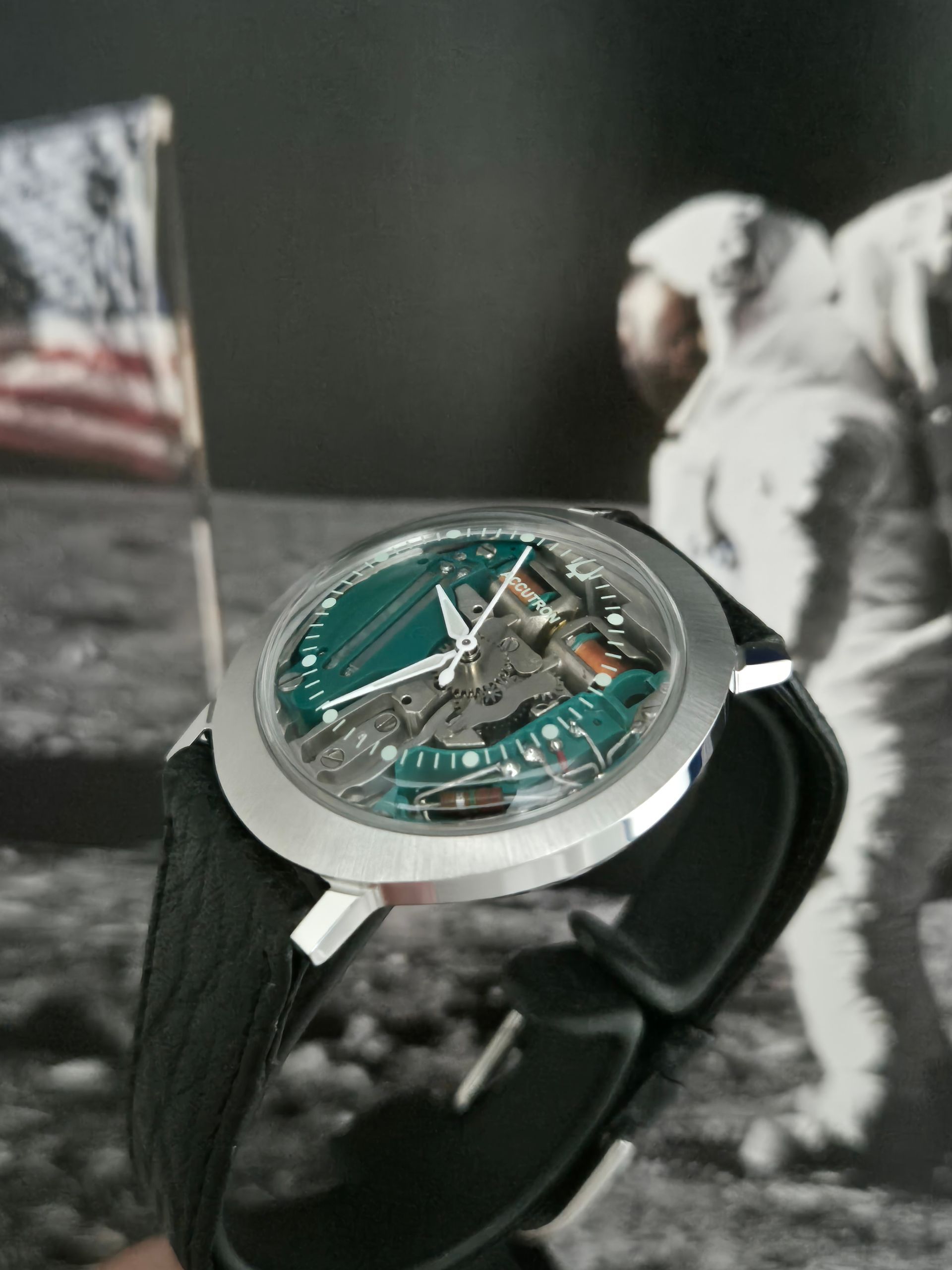 Silver wristwatch with black strap and teal face on a lunar surface backdrop