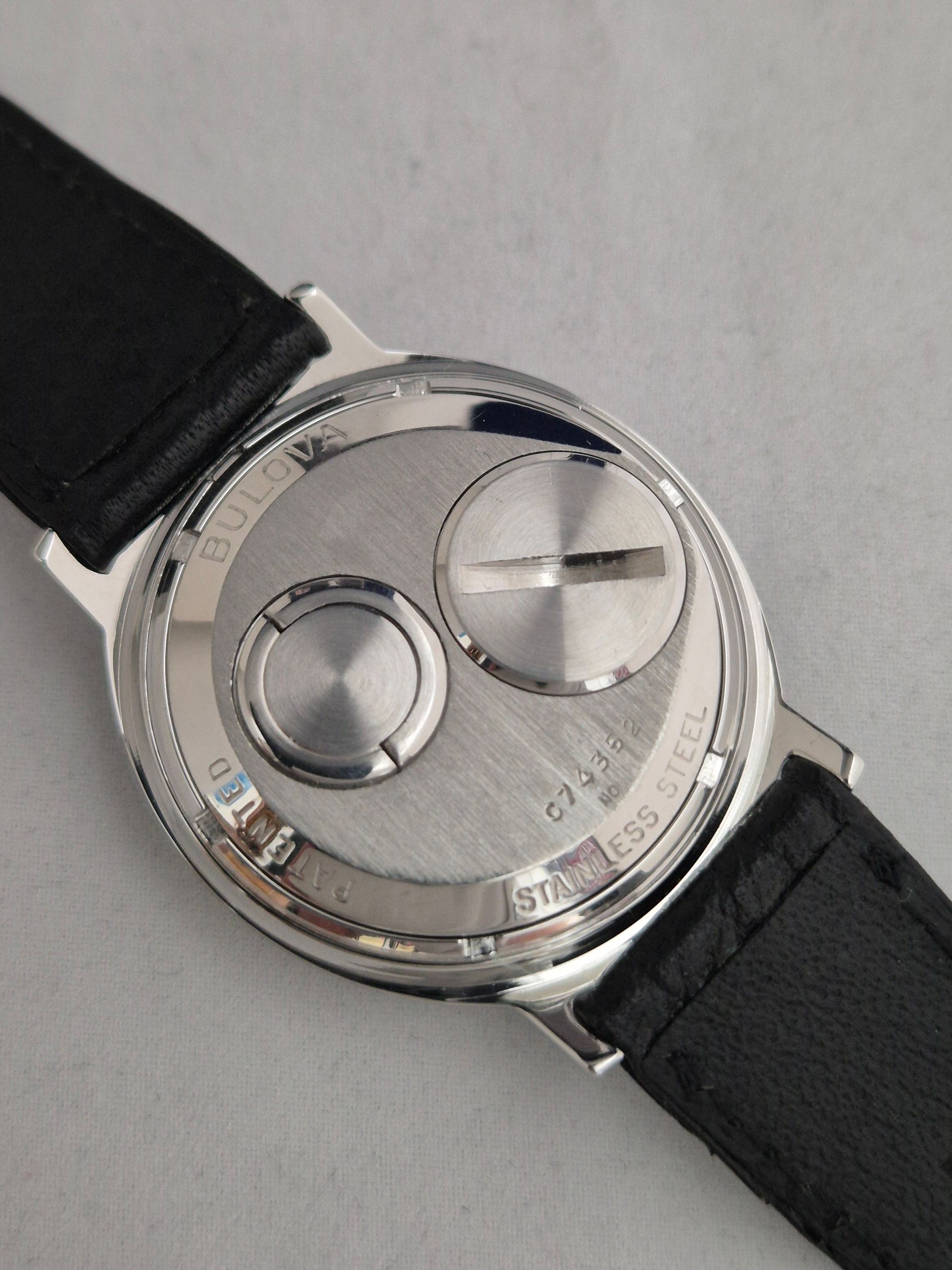 Close-up of a silver wristwatch with a black leather strap on a light surface