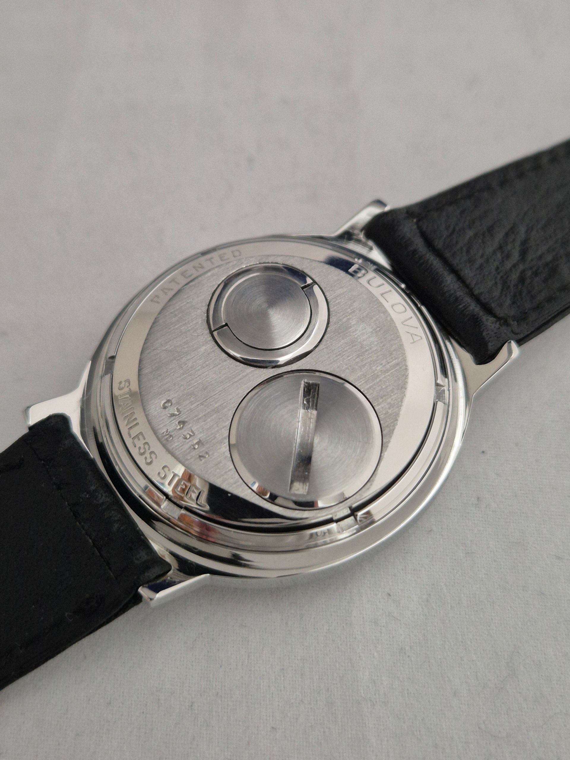 Back of a silver wristwatch with black leather strap on a light surface