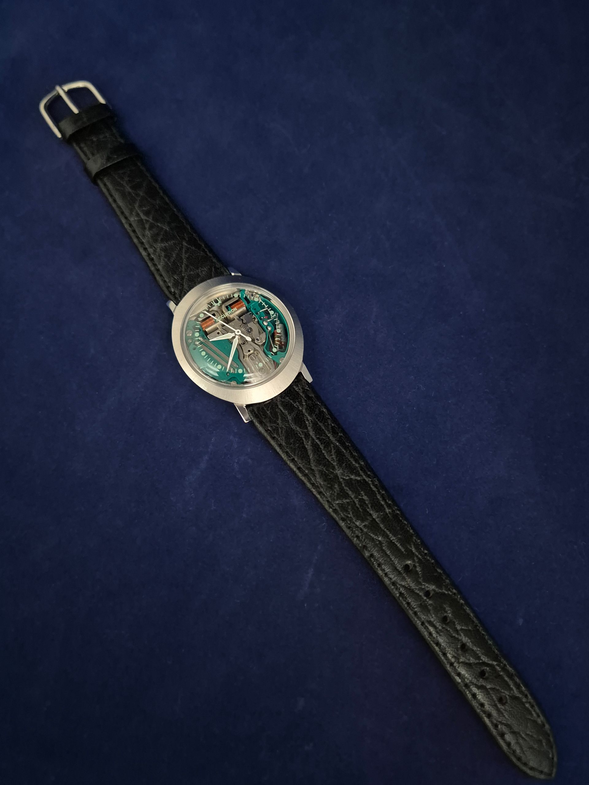 Round wristwatch with black textured strap on a blue background