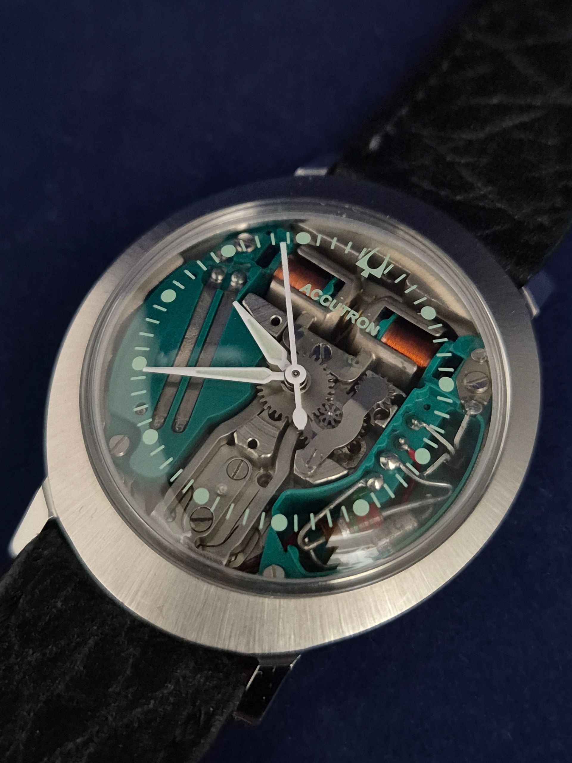 Close-up of a transparent mechanical watch with teal accents and a silver bezel on a dark strap