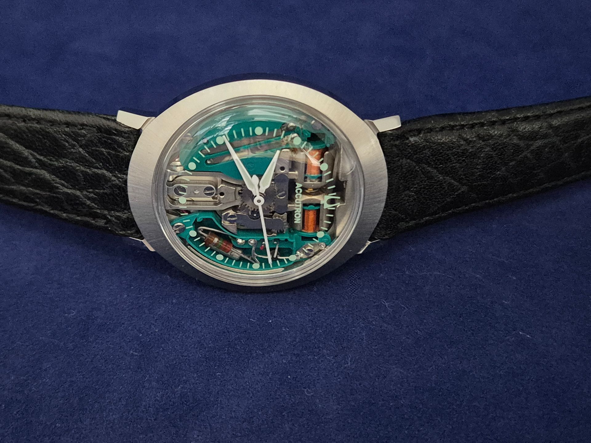Silver skeleton wristwatch with teal details on a black leather strap against a blue background