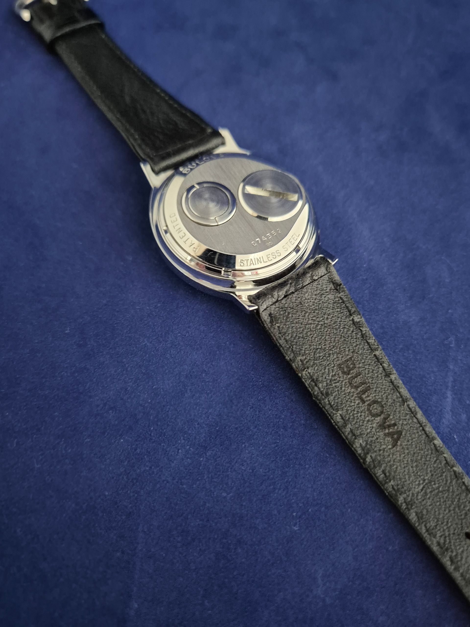 Black watch strap with a silver round face on a blue background.