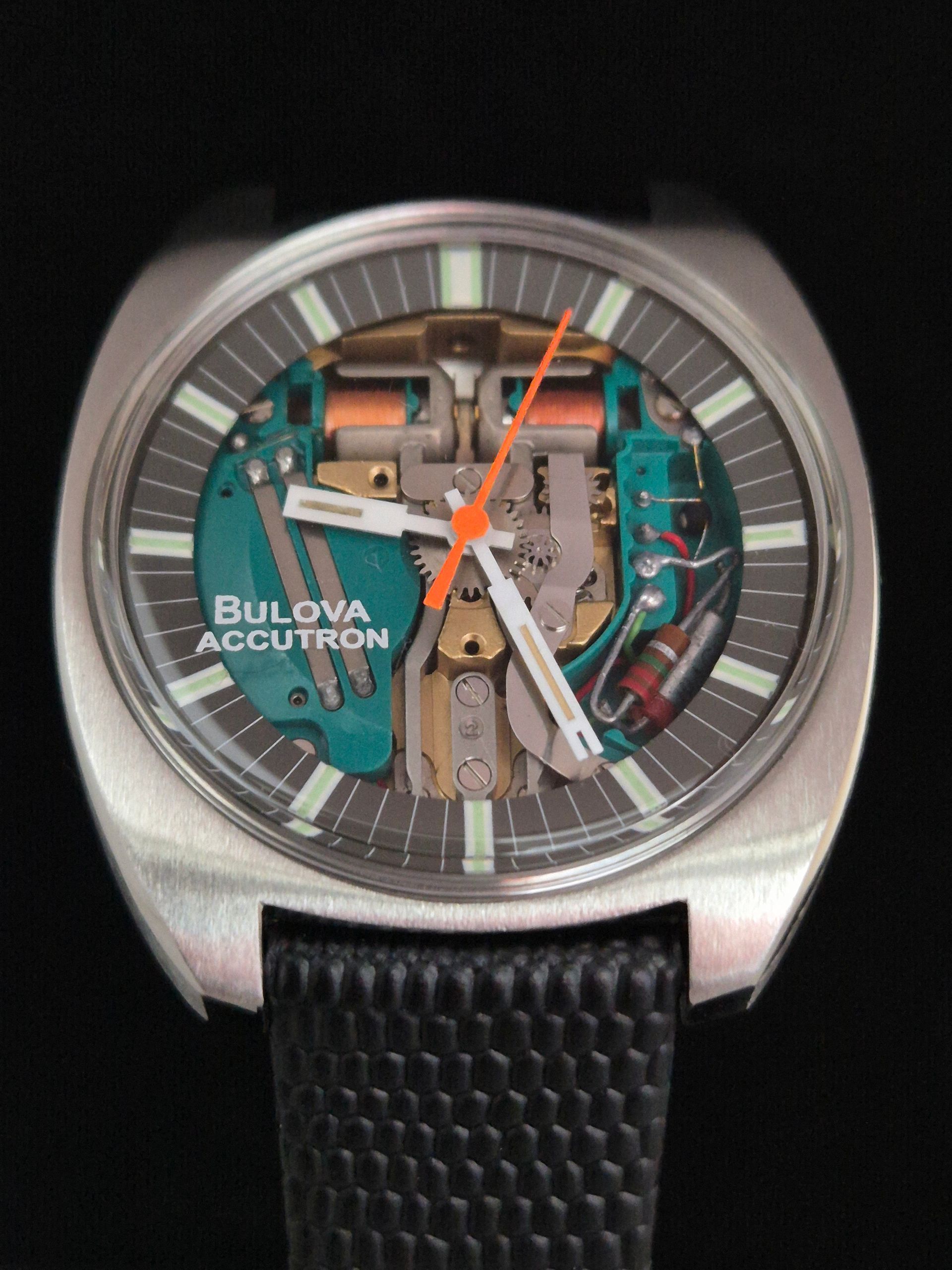 Bulova Accutron watch with visible internal mechanism, silver case, and black textured strap on a dark background