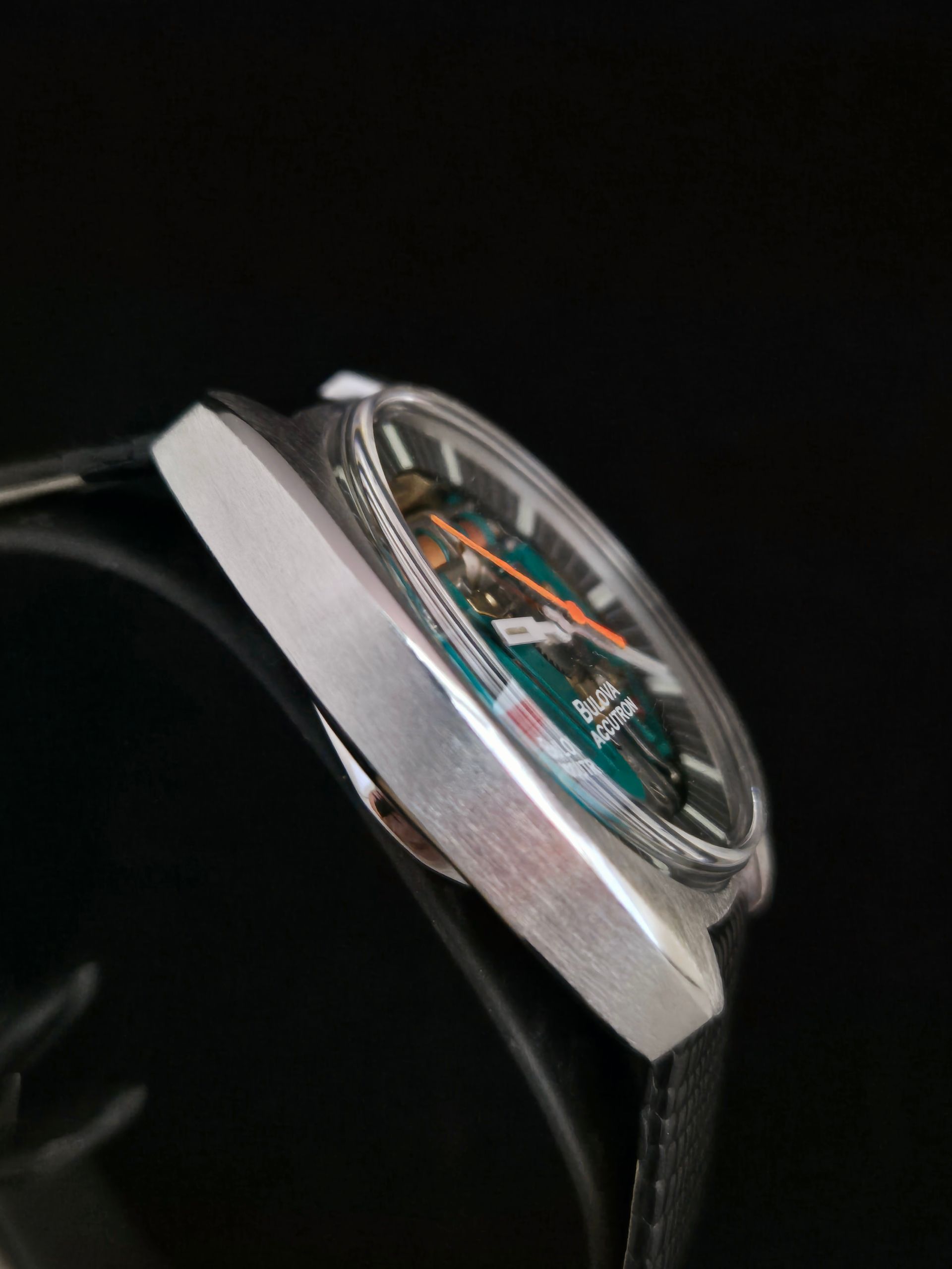 Close-up of a silver wristwatch with a black strap and visible multicolor dial details on a dark background