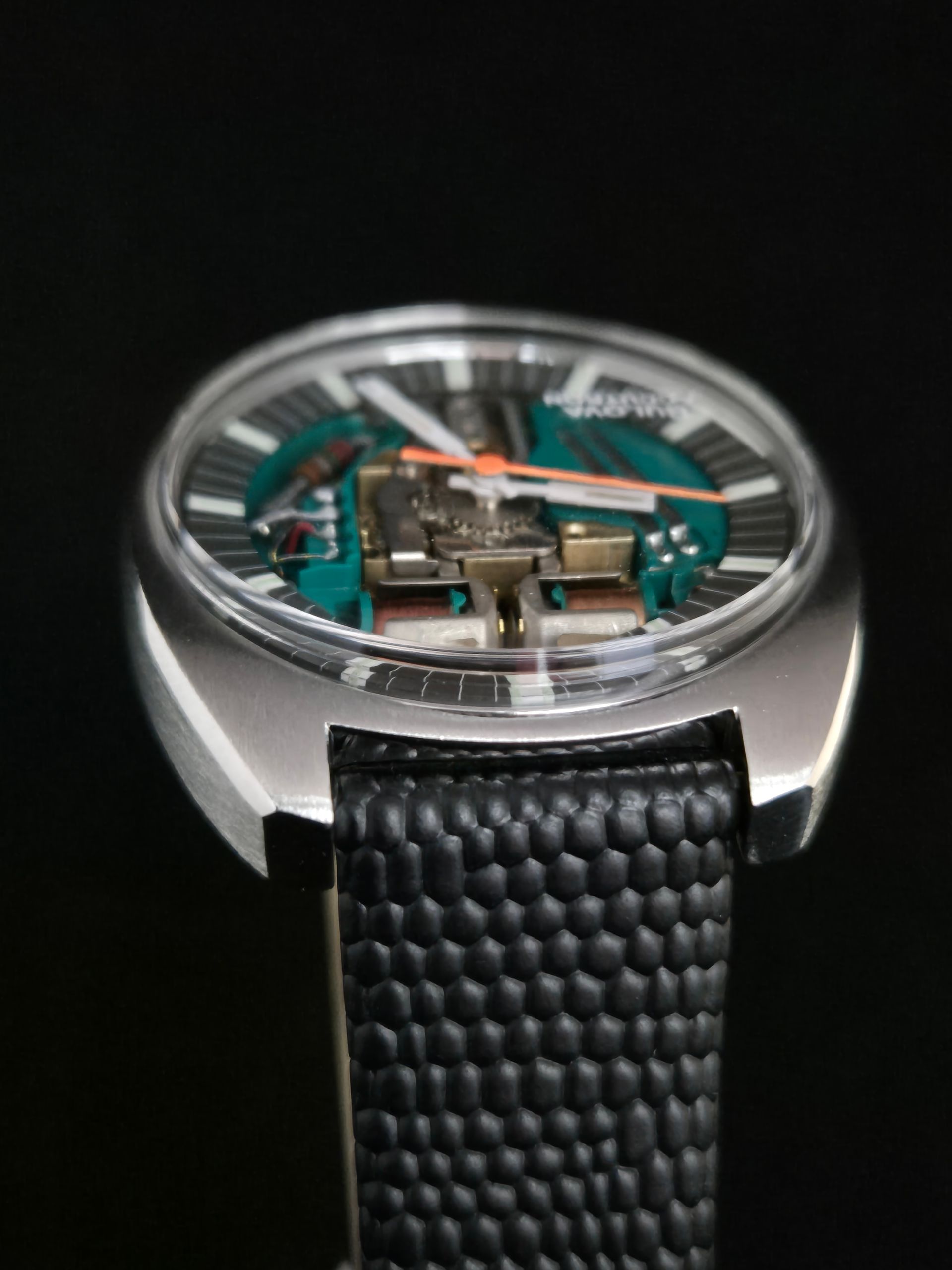 Close-up of a modern wristwatch with a black textured strap and turquoise inner details.