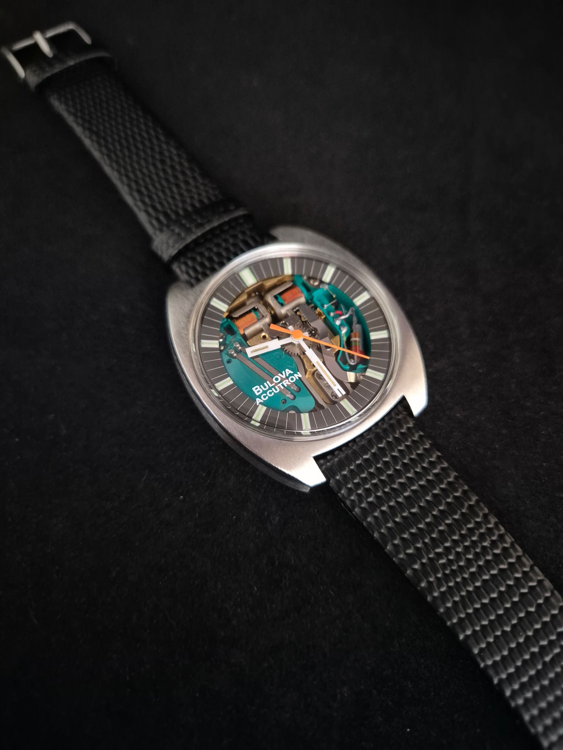 A black wristwatch with a transparent turquoise dial on a black woven strap