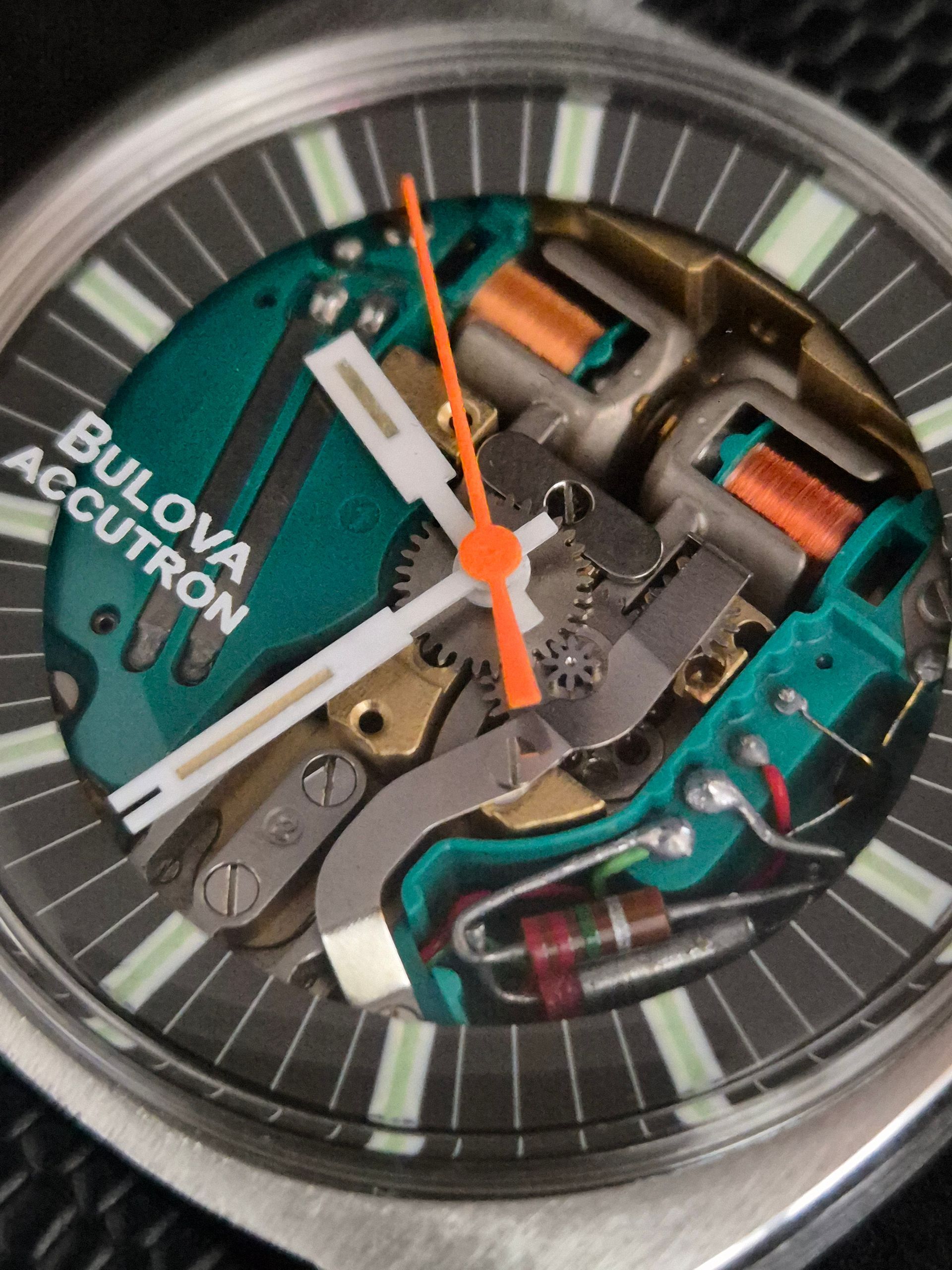 Close-up of a Bulova Accutron watch face with exposed teal and silver mechanical components and orange hands